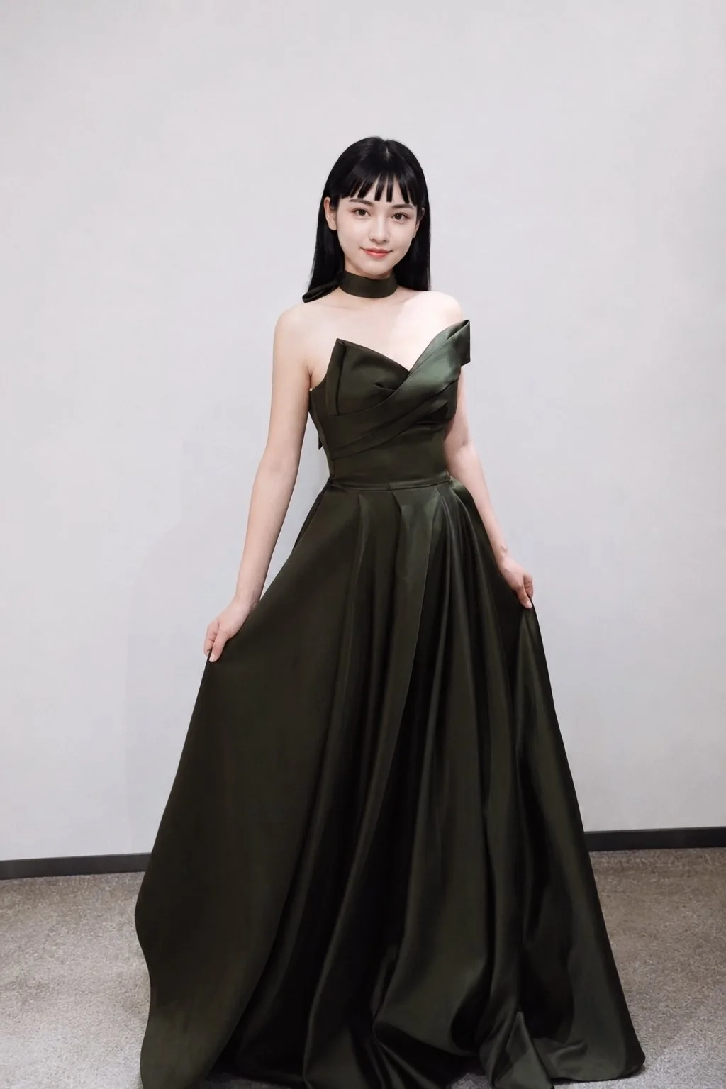 Young woman in an elegant dark green strapless ball gown, standing against a plain light-colored wall.
