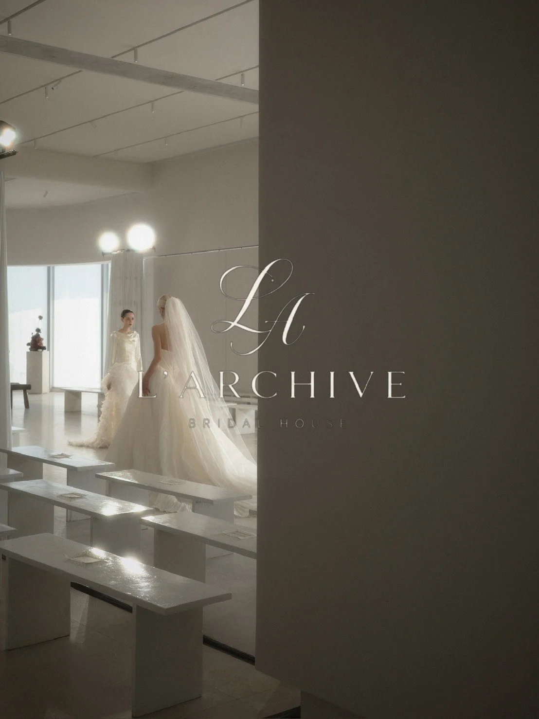 Two women in wedding dresses inside a bright, modern bridal shop, with a sign reading 'LA Archive Bridal House' partially visible in the foreground.