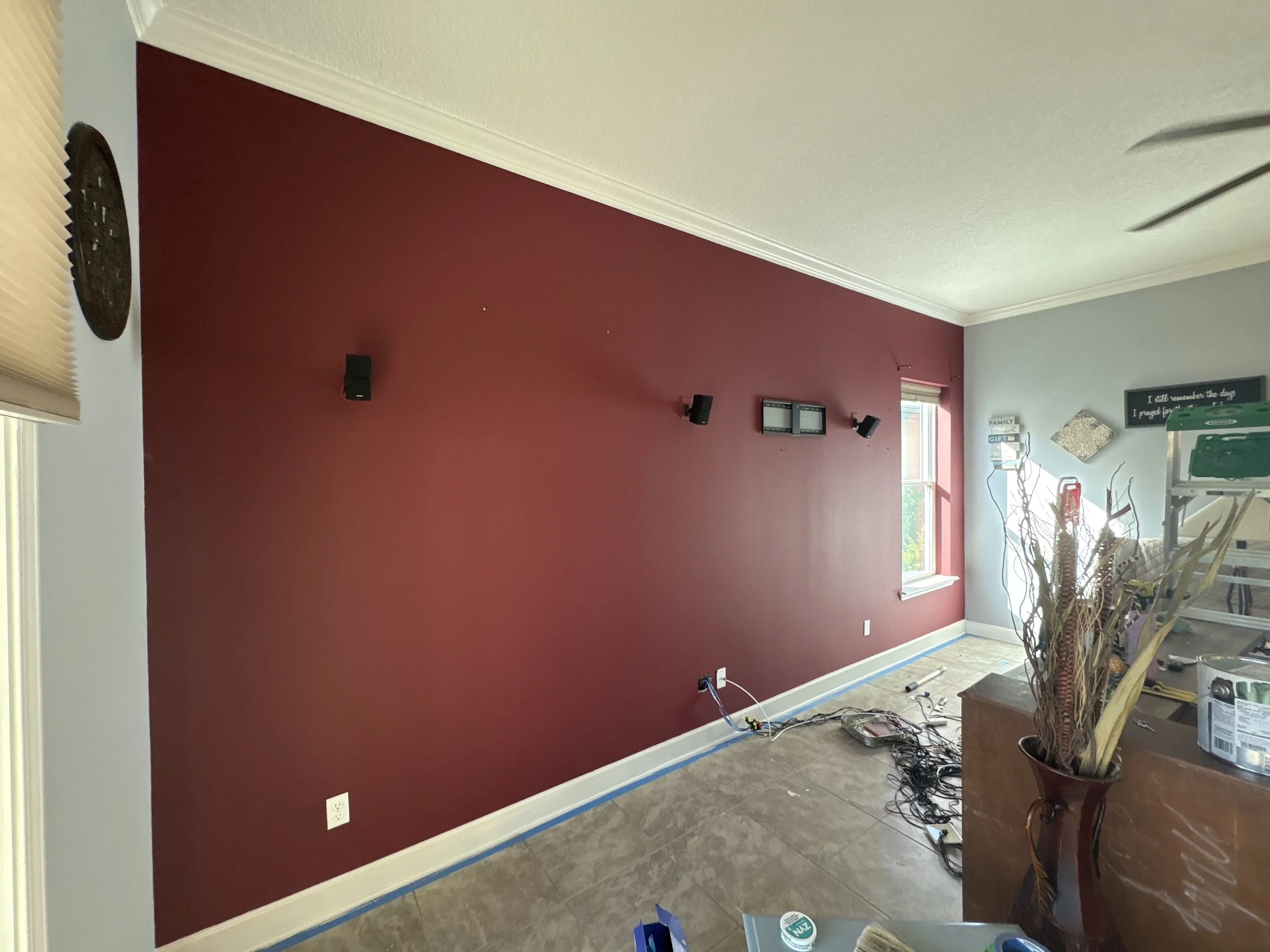 Interior of a living room with a red accent wall, decorations, and construction tools on the floor indicating ongoing renovation.
