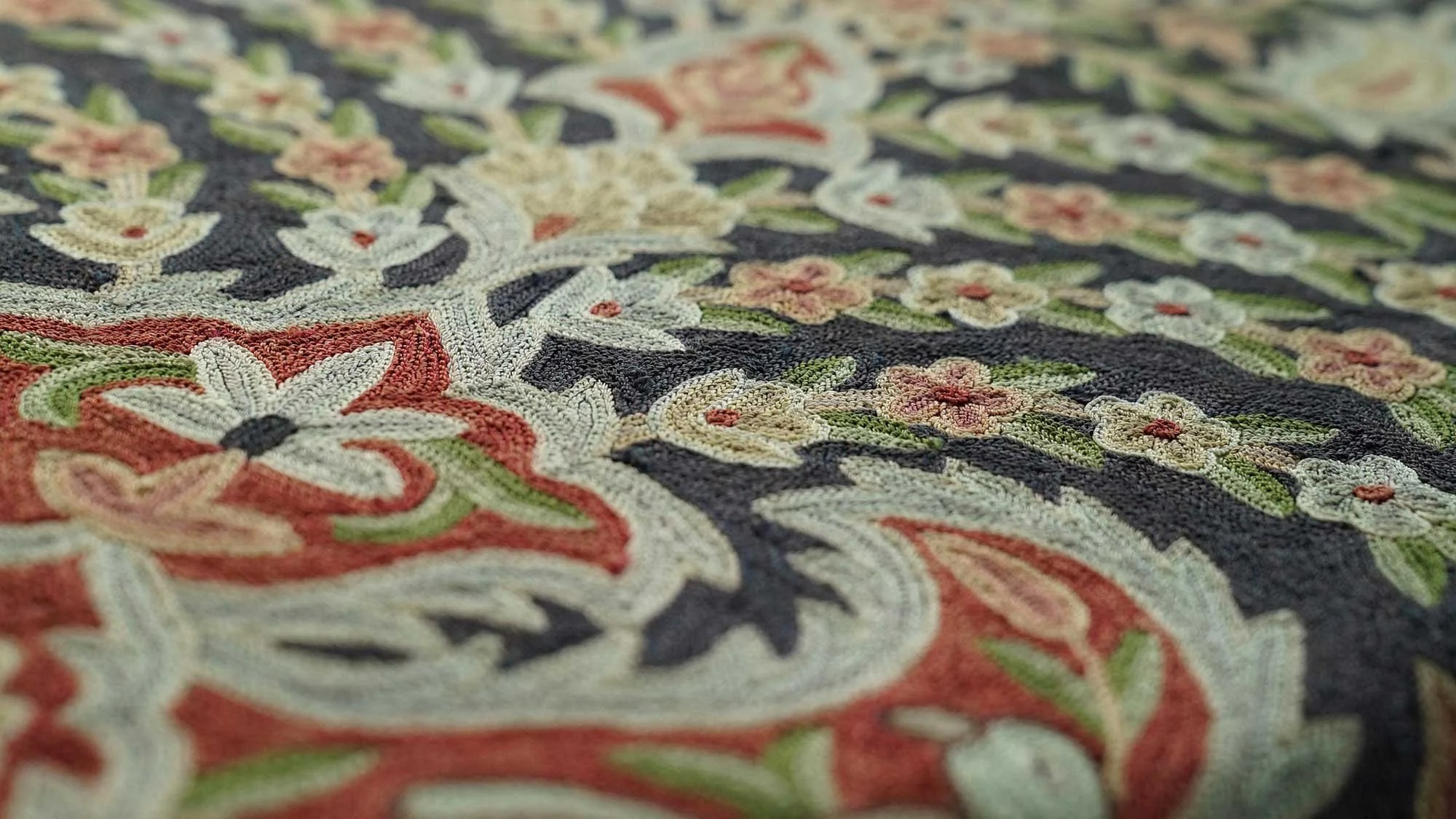 Close-up of an intricately embroidered fabric with floral and decorative patterns in colors such as white, pink, orange, green, and black.