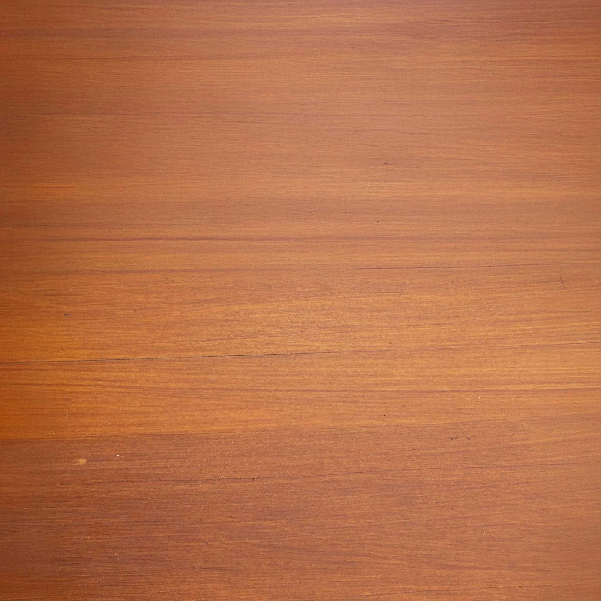 Close-up of a wooden surface with a reddish-brown hue and a smooth grain texture.
