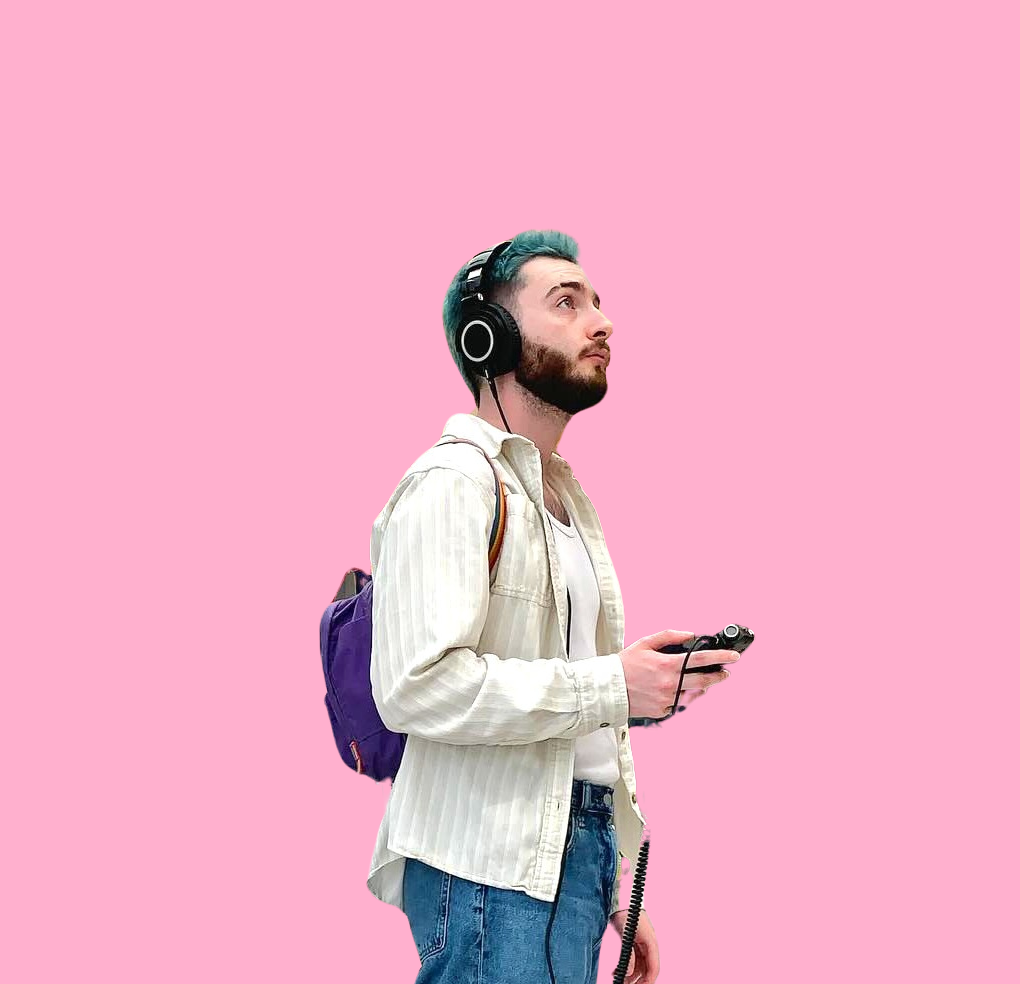 Will stands holding a portable recorder and wearing headphones while looking off into the distance over a pink background