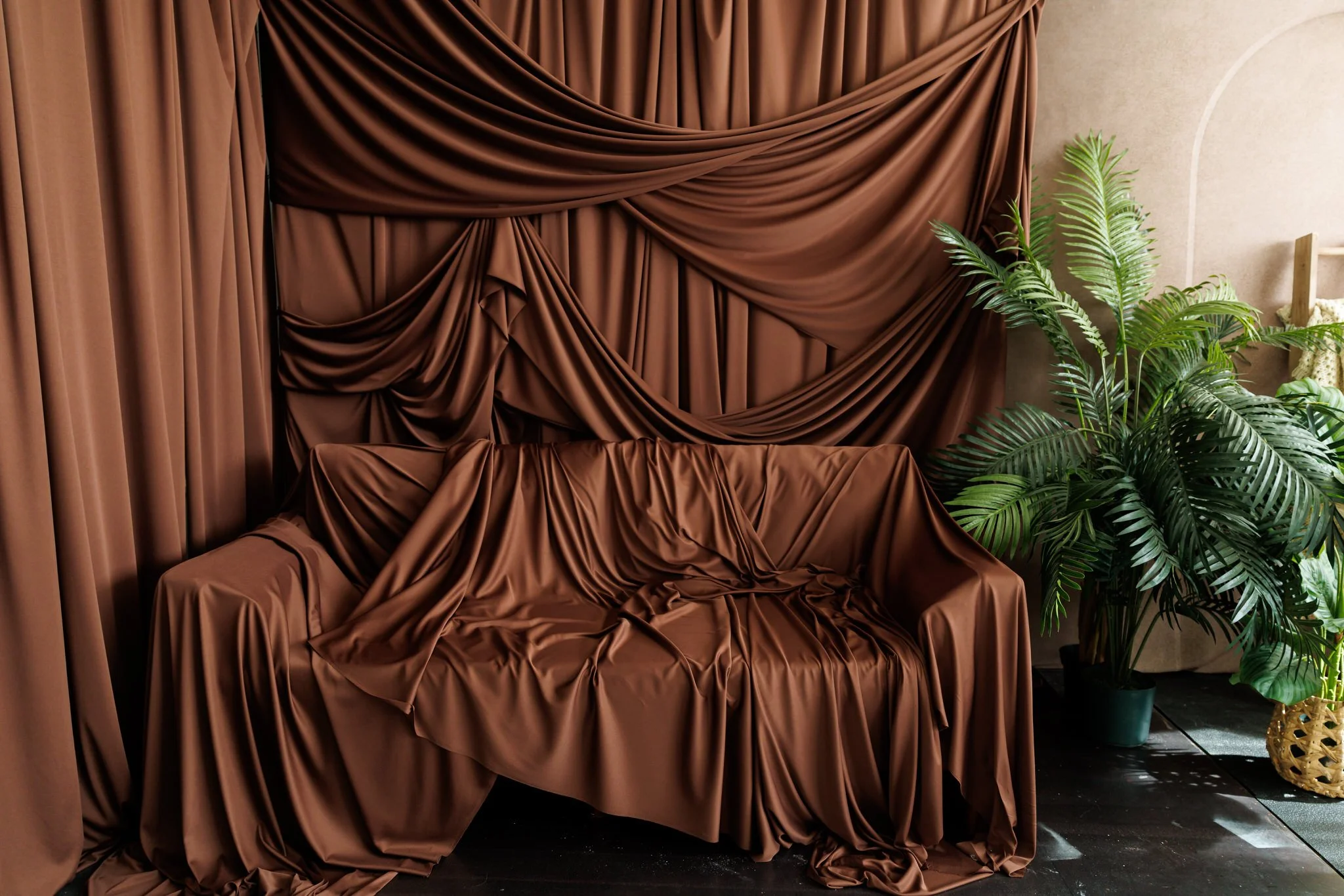 Brown fabric drapes and seat cover arranged as a backdrop, with lush green potted plants to the right.