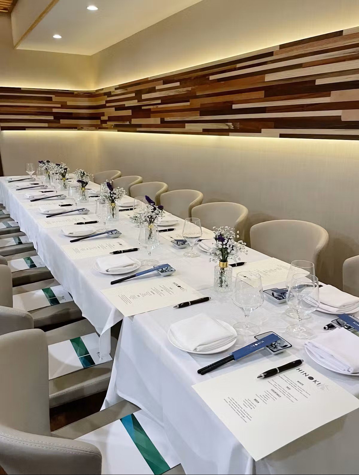 Elegant dining table set for a special event at Hinoki Burlington, featuring floral centerpieces, wine glasses, menus, and modern Japanese restaurant decor.