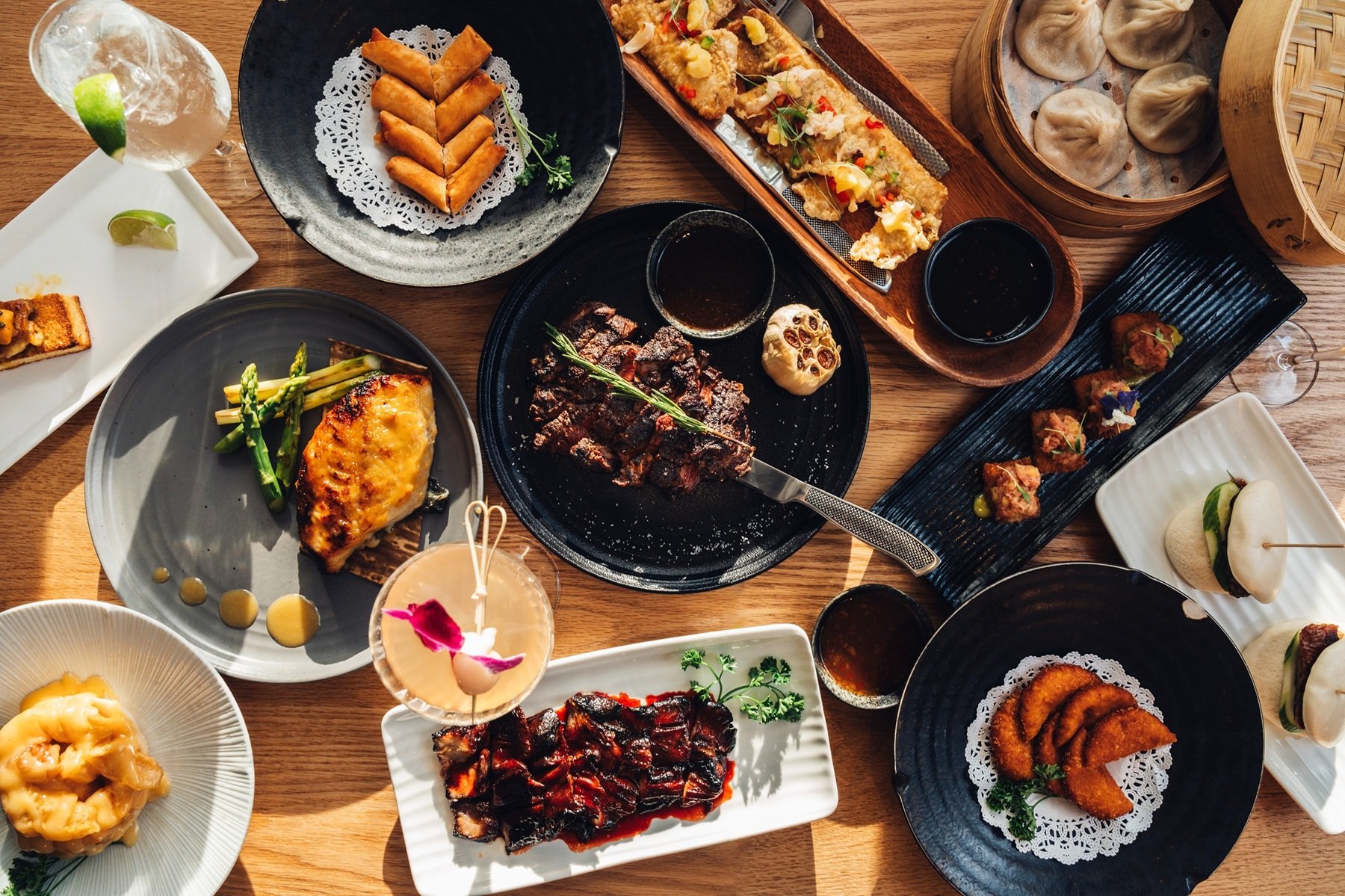 Assorted dishes at Hinoki Burlington, including dumplings, spring rolls, grilled steak, fried fish, vegetables, sauces, and drinks.