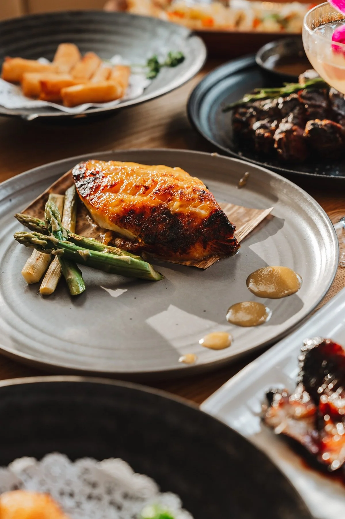 Grilled salmon with asparagus and sauce served alongside other dishes at Hinoki Burlington.