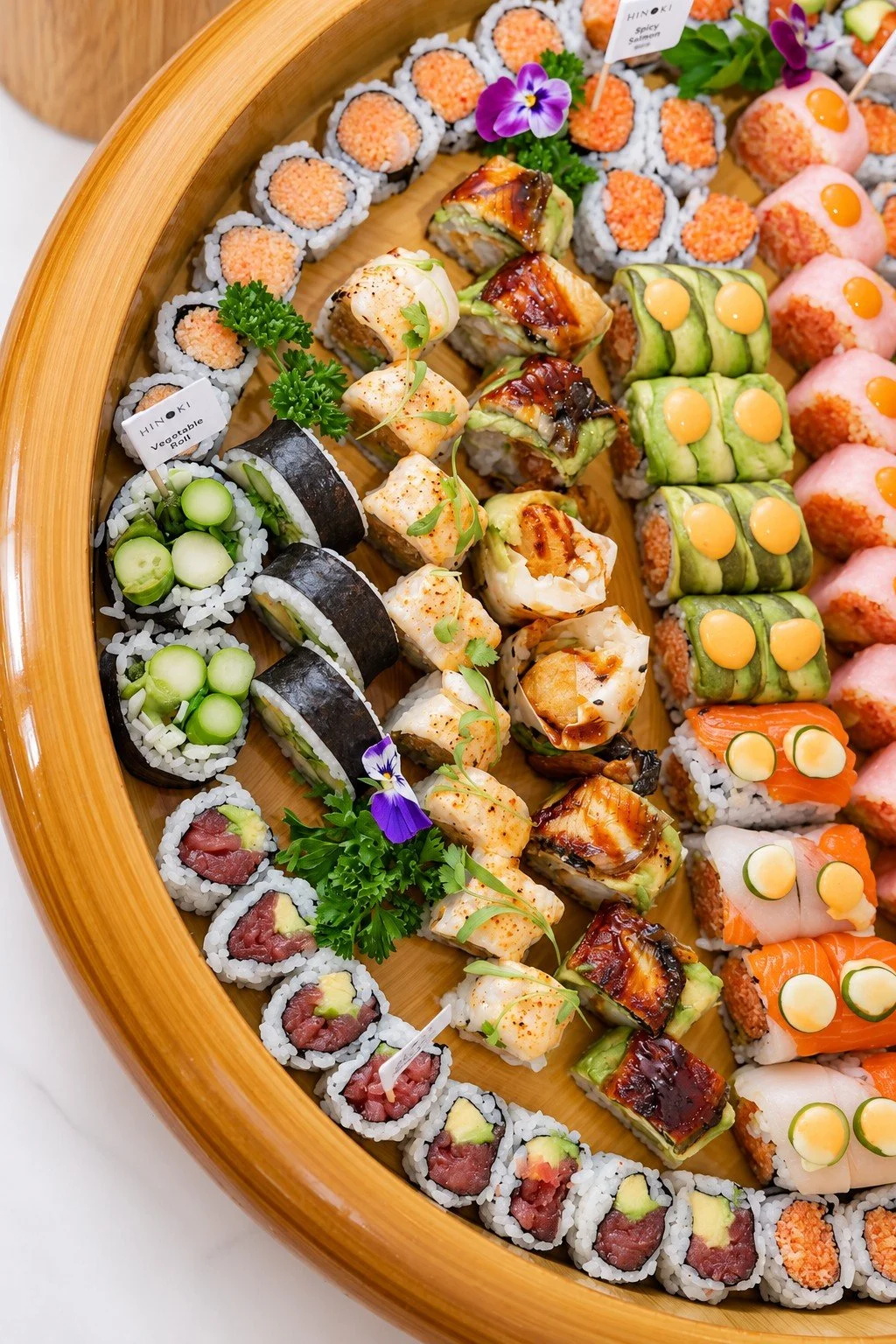 Assorted sushi rolls on a wooden platter with edible flowers and garnishes at Hinoki Burlington.