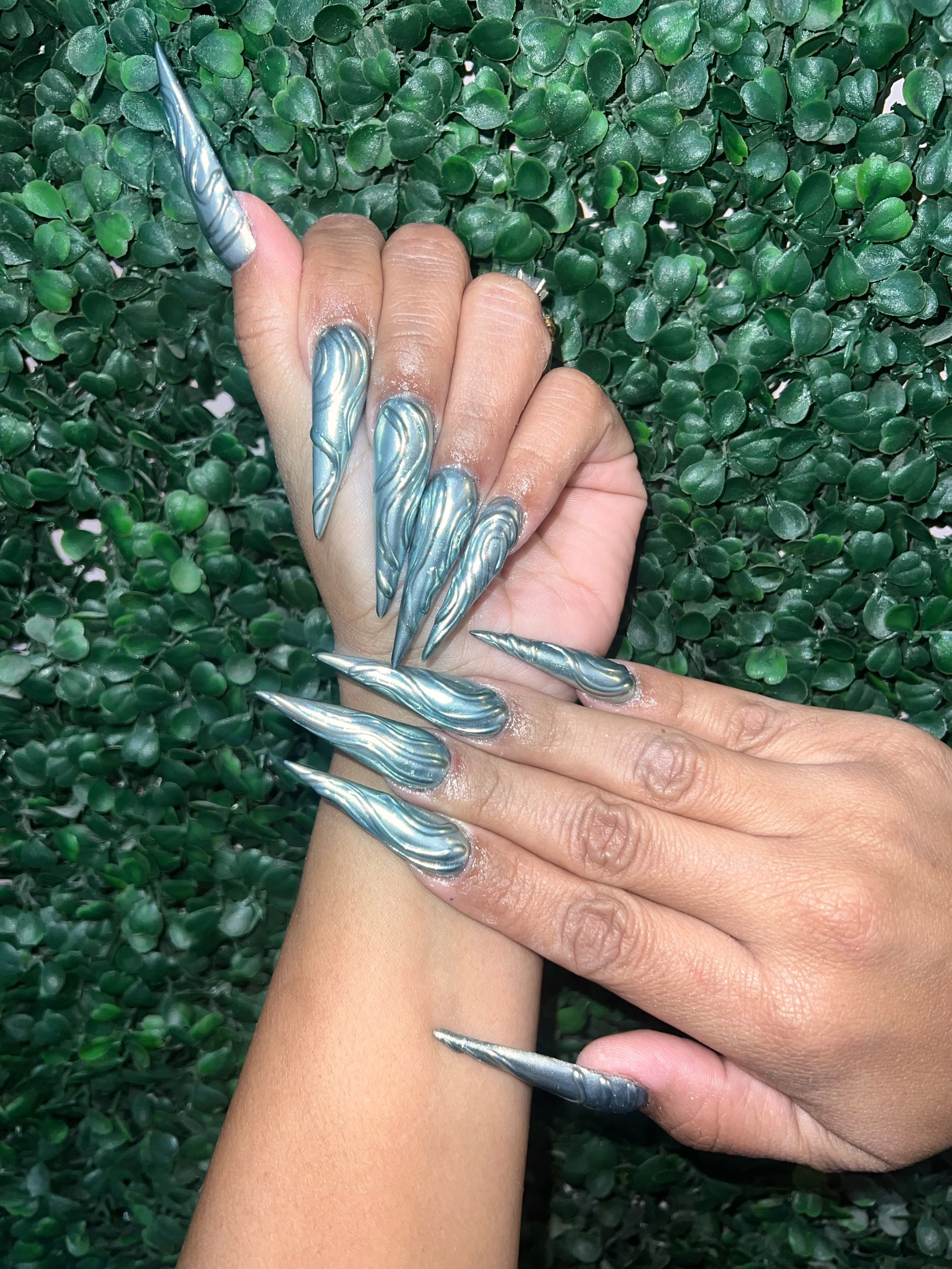 Metallic silver stiletto nails with sculpted wave details.