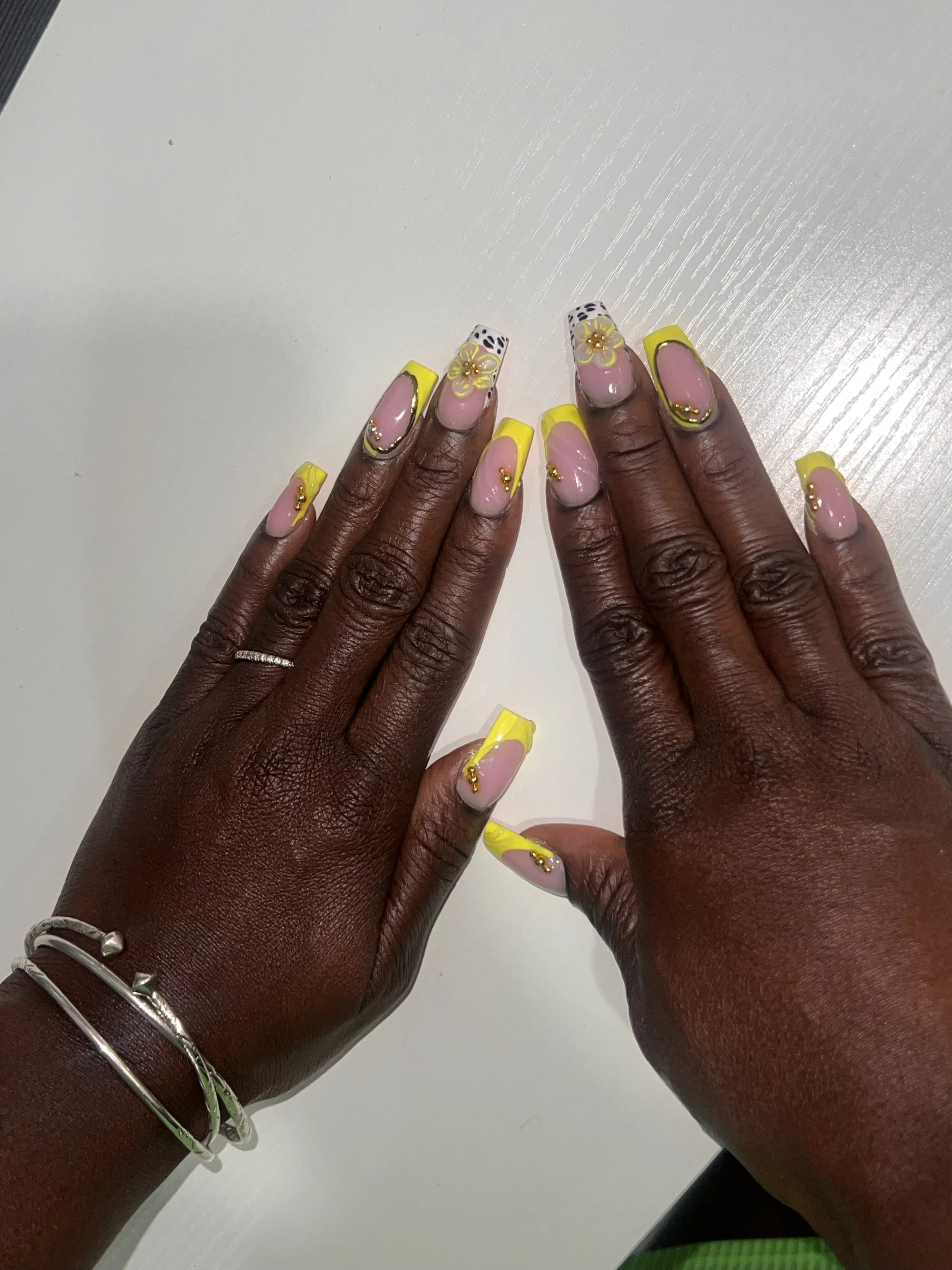 Yellow French-tip nails with floral and gold accents.