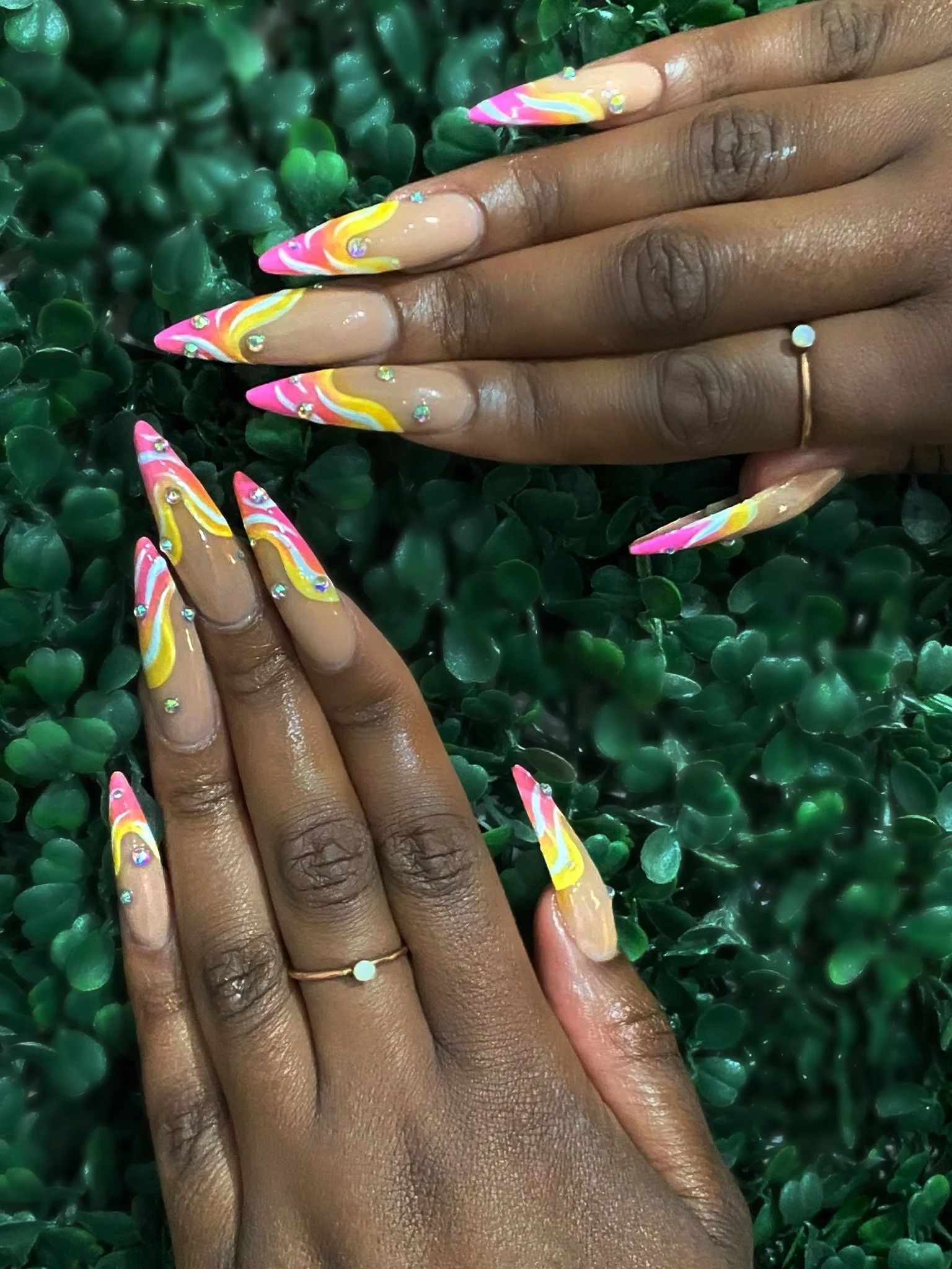 Colourful pink, orange and yellow swirl nail art with rhinestones.
