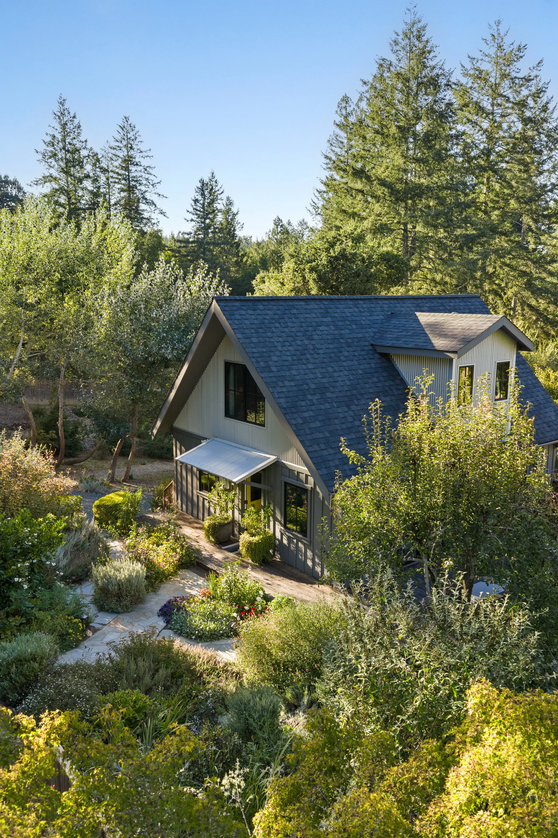 A house with a blue roof surrounded by lush greenery and trees in a garden on a sunny day.