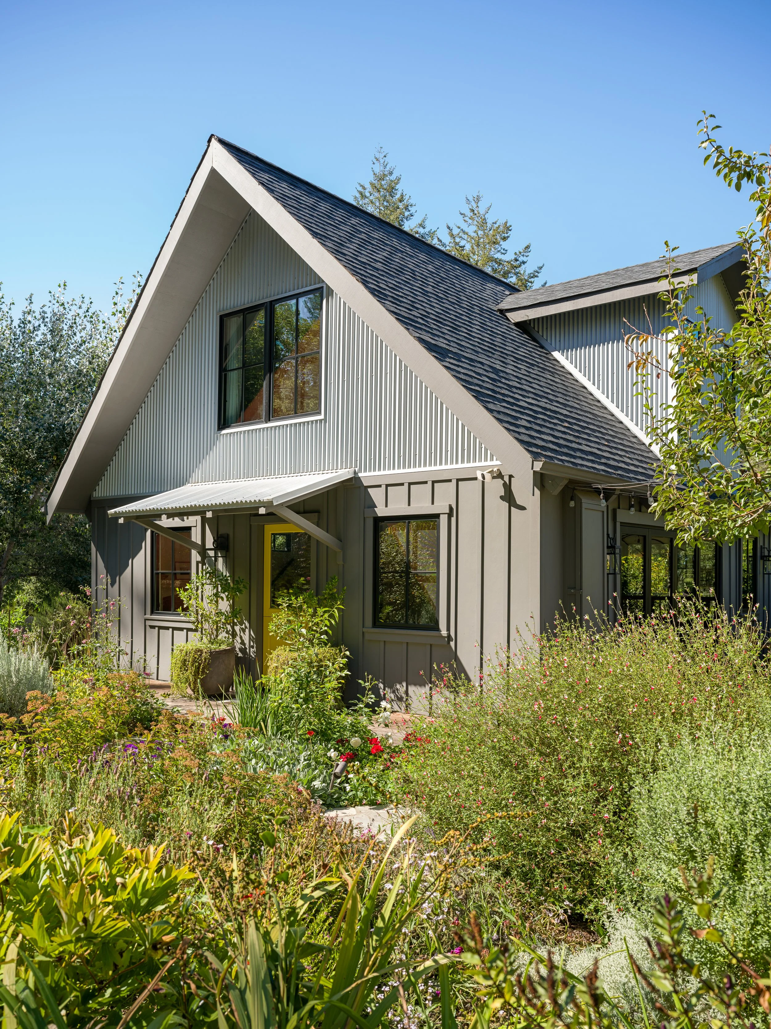 A modern house with a steeply pitched roof, large windows, and a landscaped garden with various plants and flowers in the foreground.