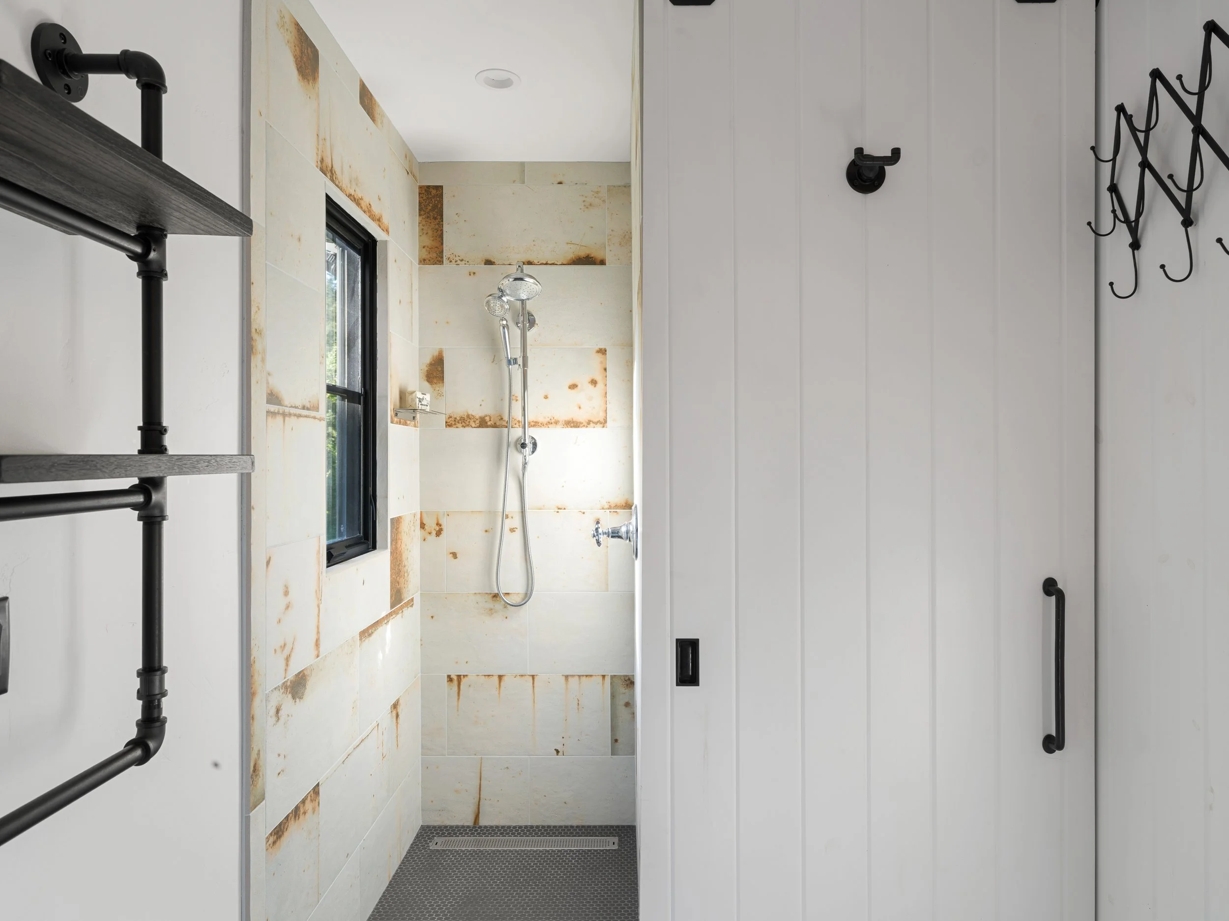 Modern bathroom shower with marble tiles, black fixtures, and a window, featuring rust stains on the tiles.