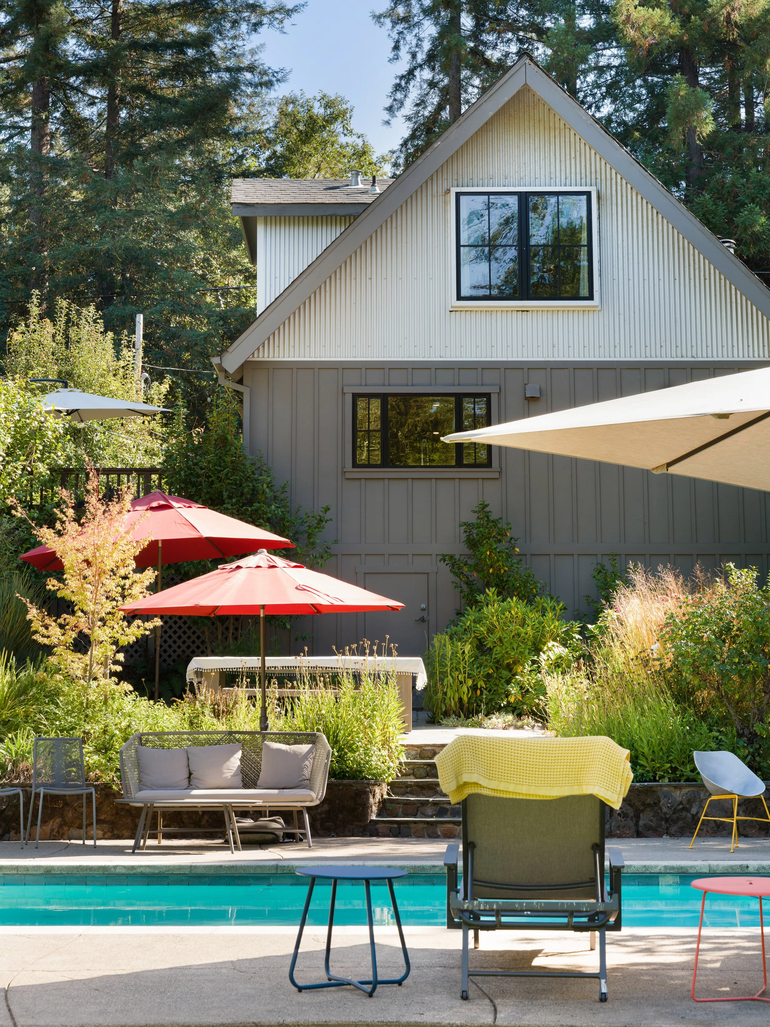 Backyard with patio furniture, umbrellas, house, trees, swimming pool, and outdoor chairs and tables.
