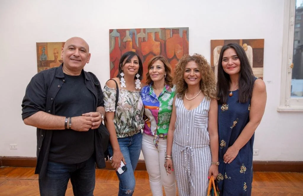 Five people, three women and two men, standing together in an art gallery with paintings on the wall behind them.