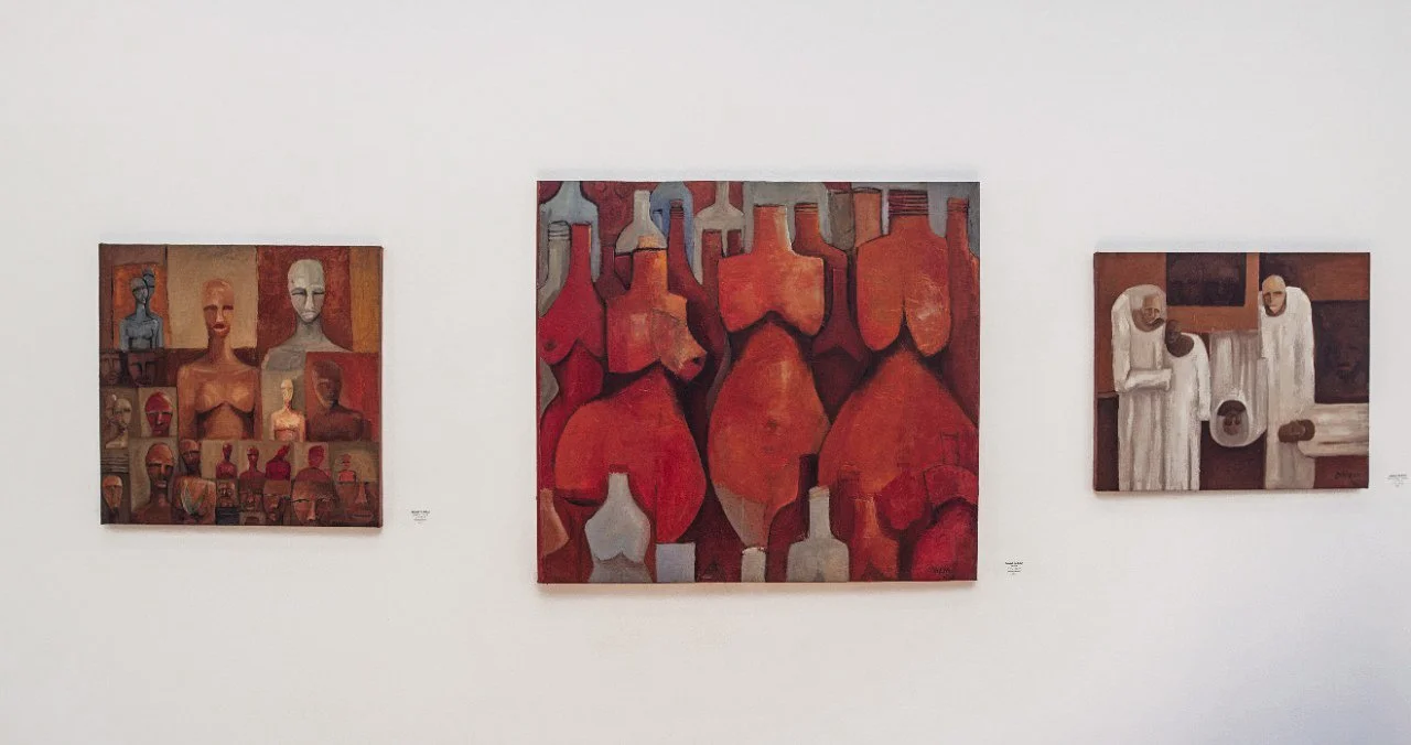 Three paintings displayed on a white wall, depicting abstract and figurative art in warm tones.