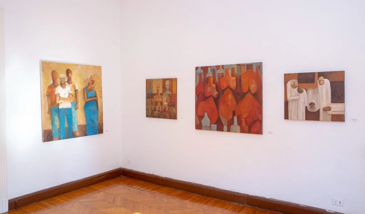 An art gallery featuring four paintings on white walls, with hardwood floors.