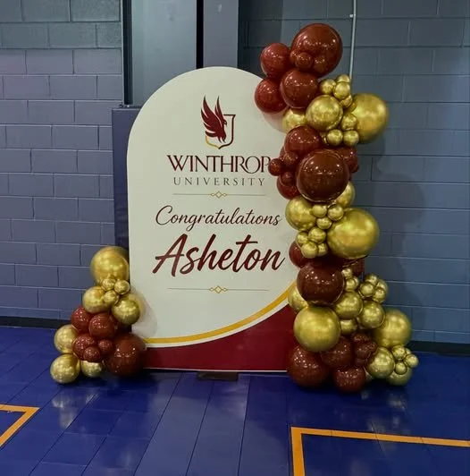 Winthrop University congratulation sign for Asheton, decorated with red and gold balloons.