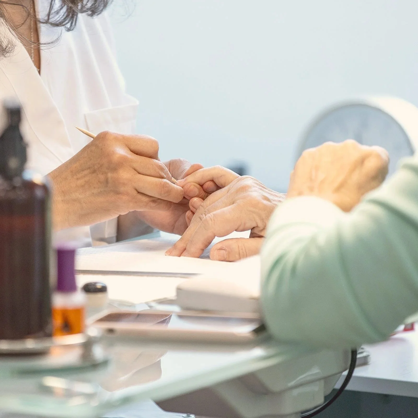 A healthcare worker in white scrubs administering a fingernail test to an elderly person with wrinkled hands.