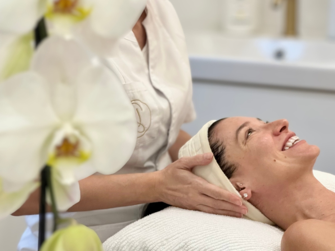 A woman receiving a facial massage while lying on a spa table, with orchids in the foreground.