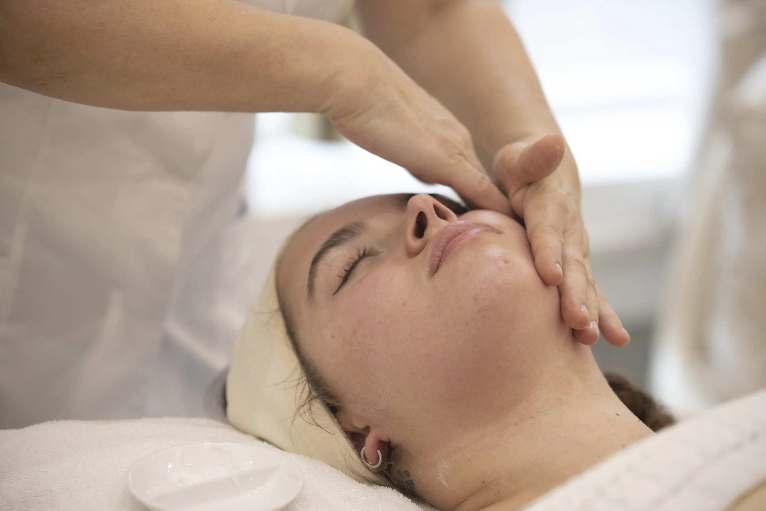 A woman receiving a facial massage while lying down with closed eyes.