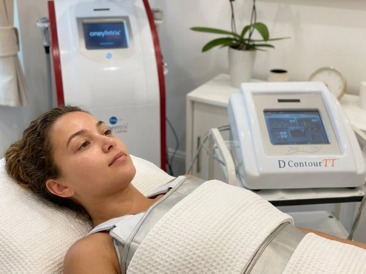 A woman lying on a treatment bed with medical devices and equipment nearby, including a machine labeled 