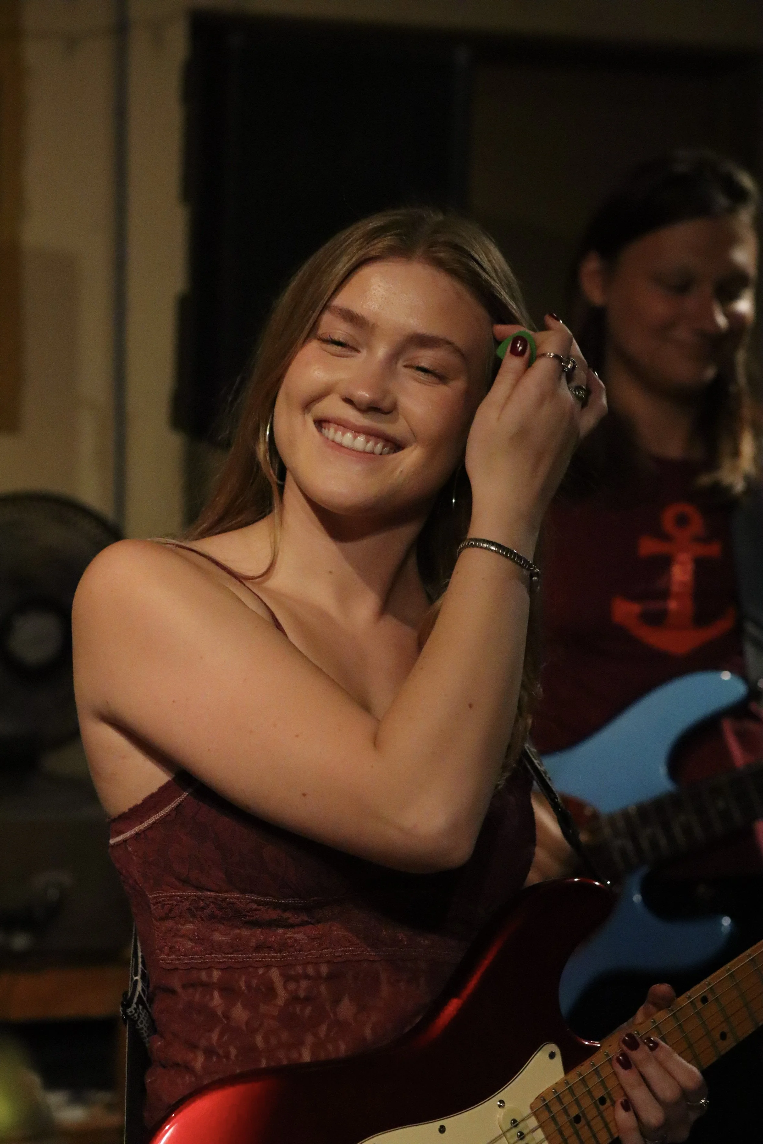 A woman smiling while playing an electric guitar during a live music performance.