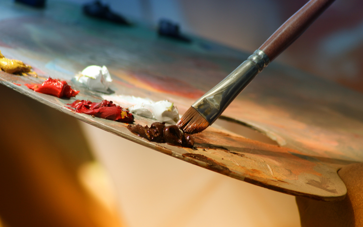 Close-up of artist's palette with various colors of paint and a paintbrush resting on it.
