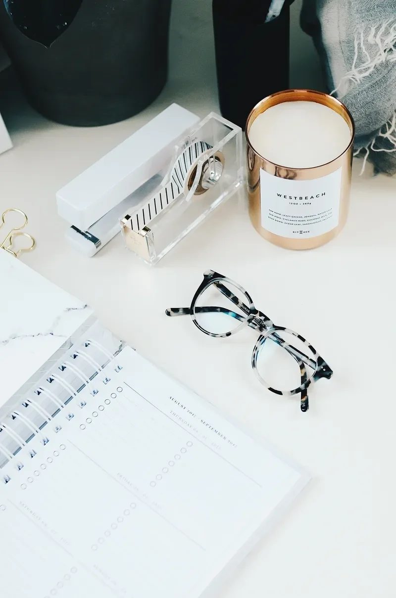 Desk with a candle, glasses, planner, and decorative objects.