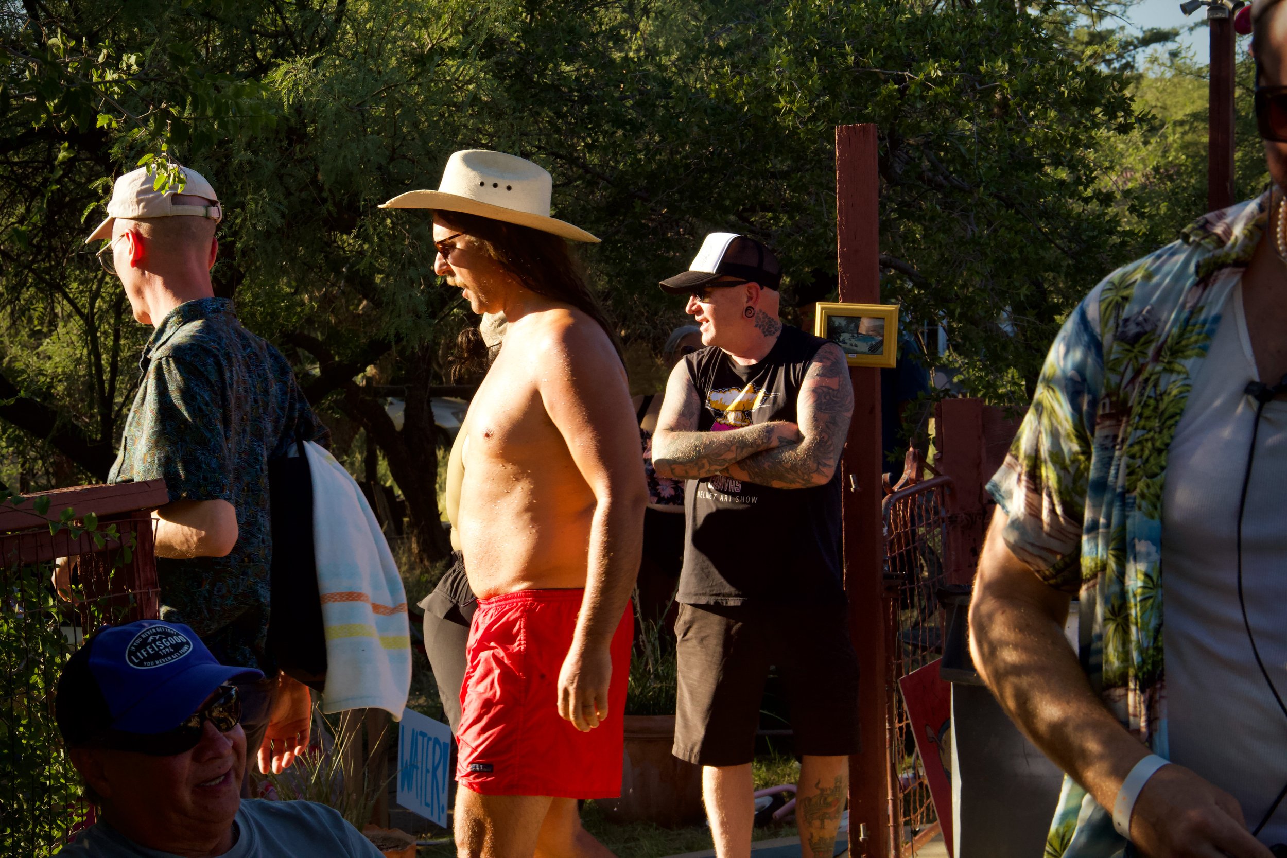 Group of people outdoors, some wearing hats, engaged in conversation on a sunny day.