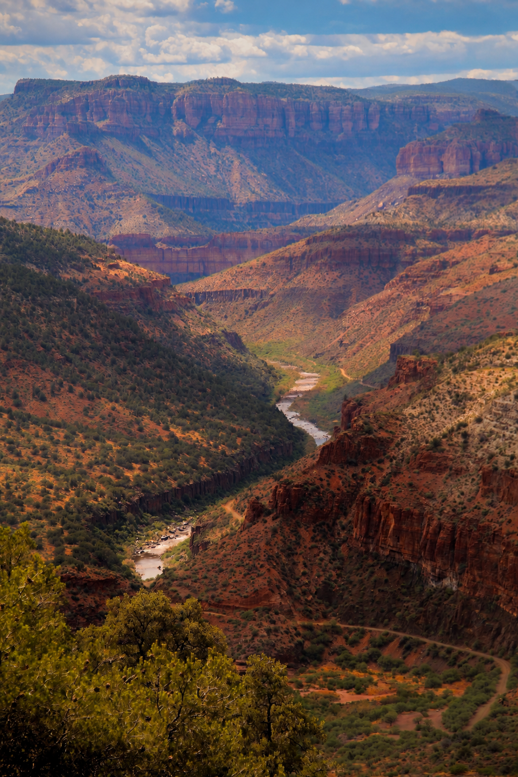 Scenic view of the Grand Canyon with layered red and orange cliffs, a winding river at the bottom, and a partly cloudy sky overhead.