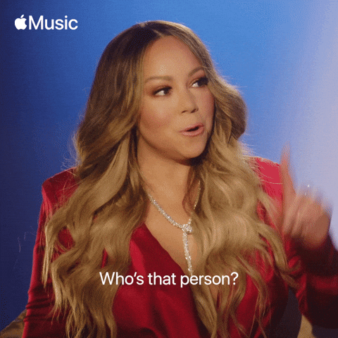 A woman with long wavy hair wearing a red blazer and a diamond necklace, gesturing while speaking in an interview setting with a blue background, featuring the Apple Music logo.