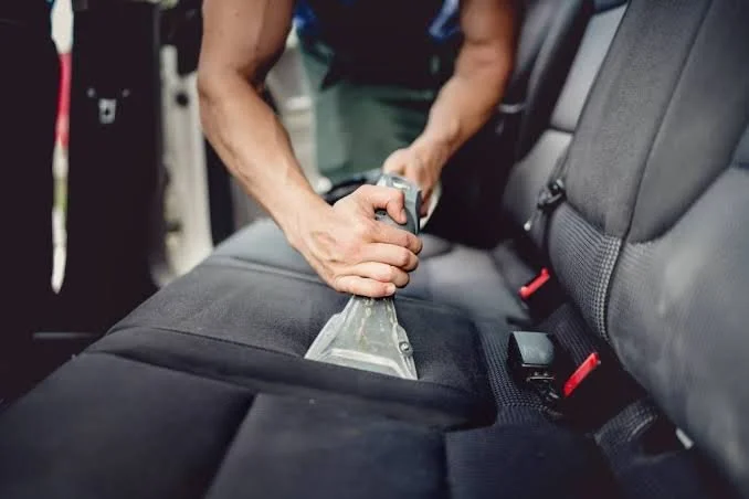 Person cleaning a car interior with a vacuum cleaner on the back seat.