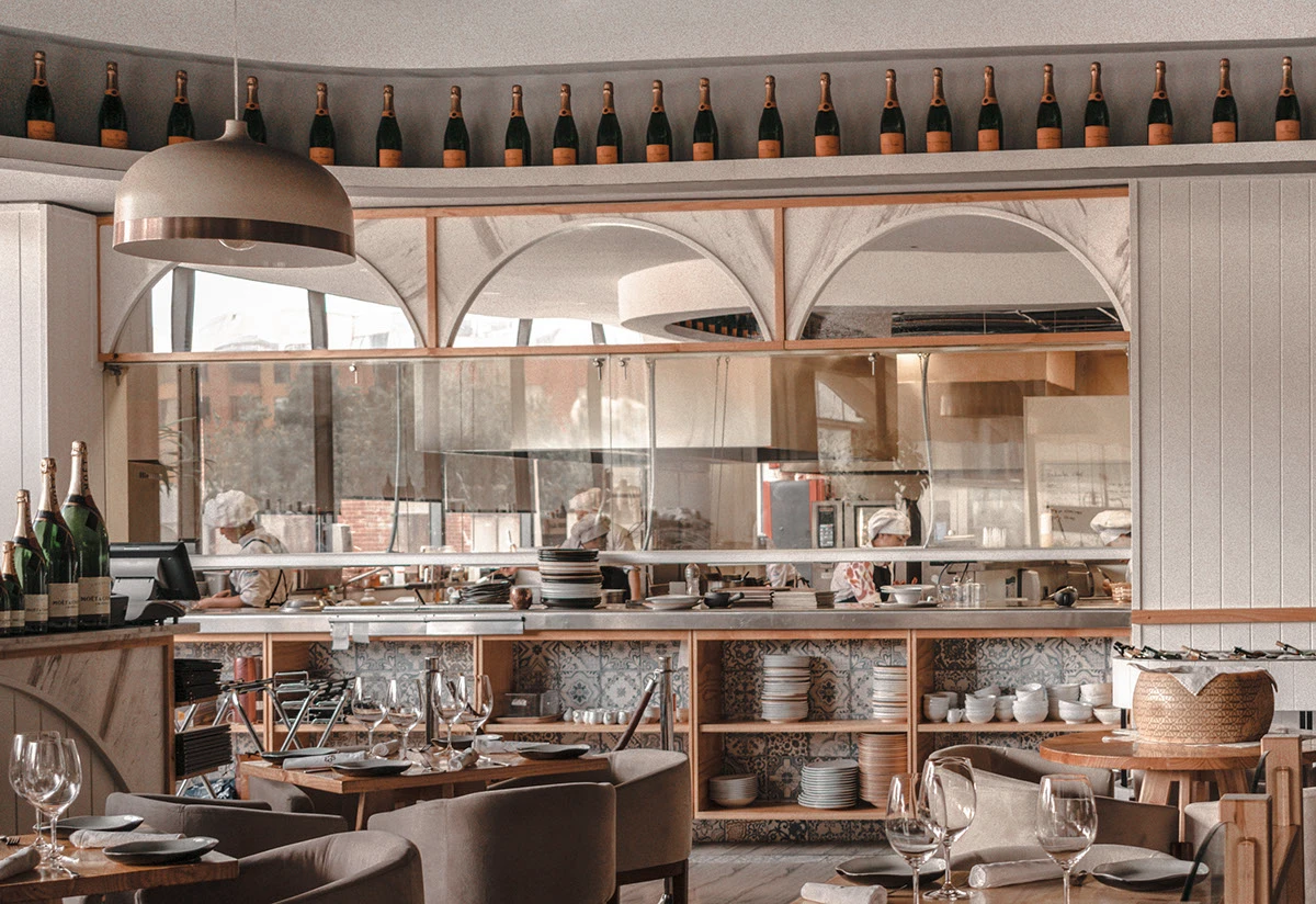 Restaurante con cocina a la vista, botellas de champagne, mesas organizadas, vajillas y copas