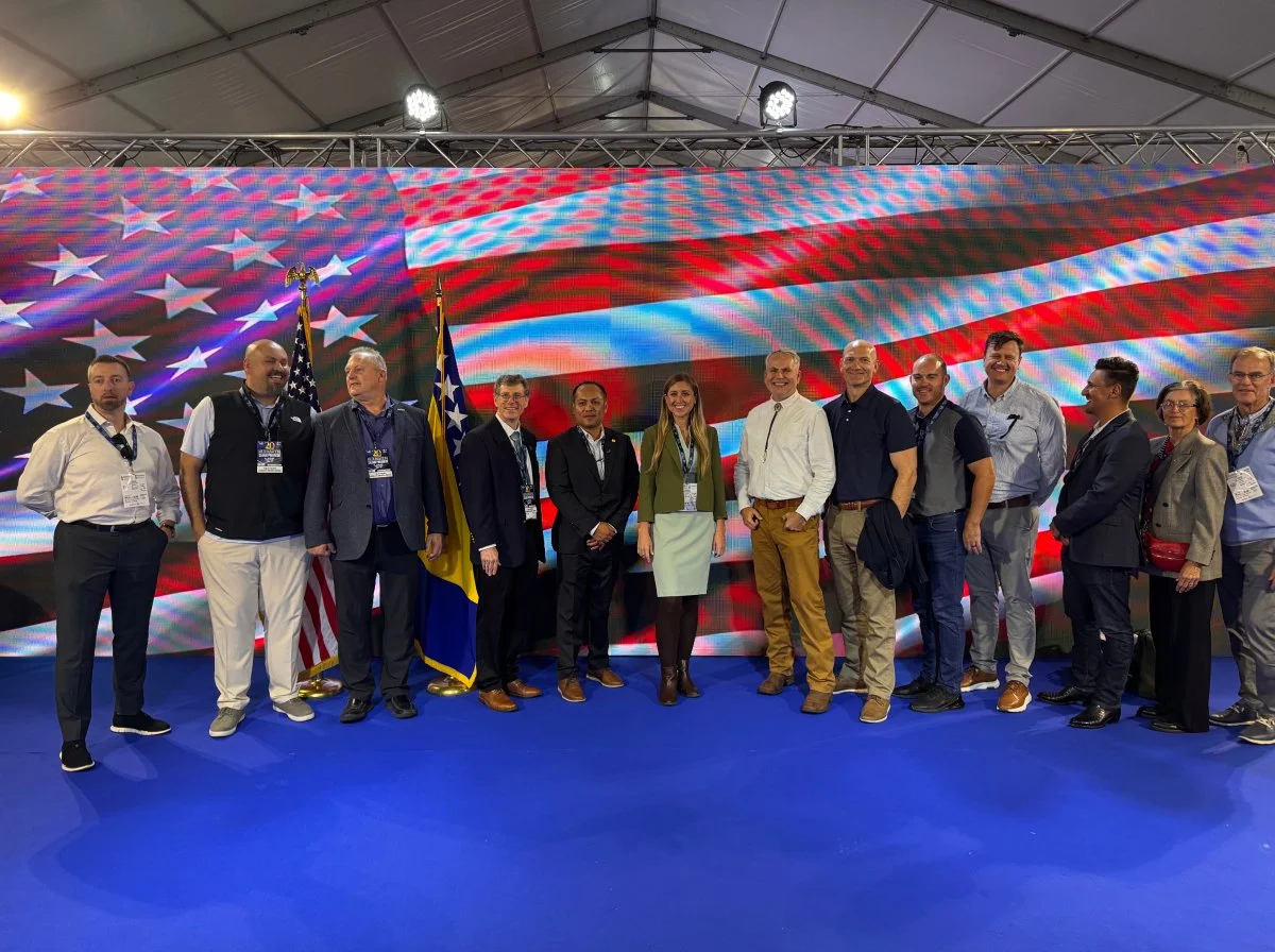 Group of diverse people standing in front of a large American flag display at an event.