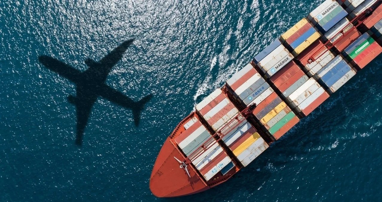 A cargo ship sailing on the ocean with its shadow cast on the water below.