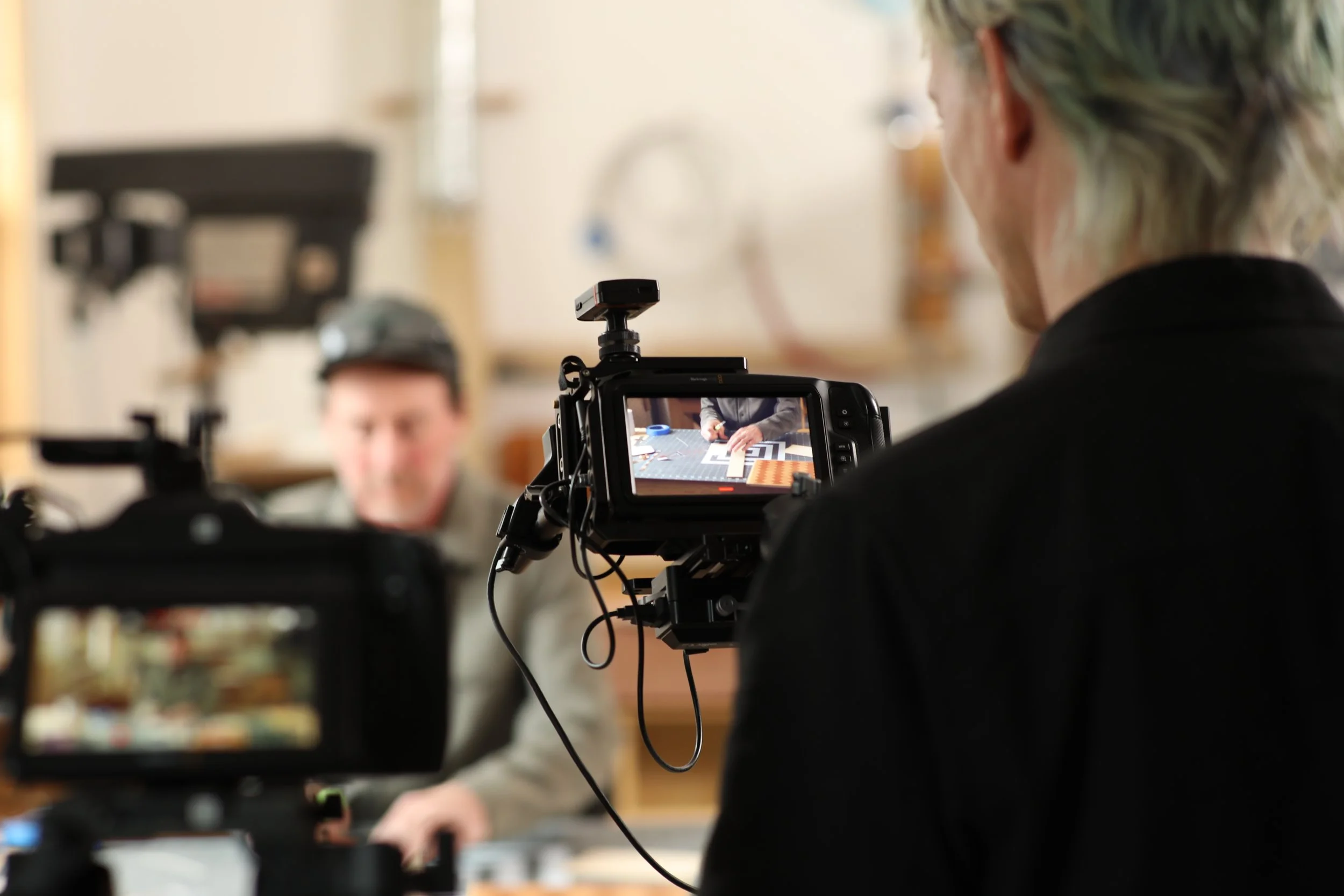 Person filming a person working on a craft project at a table with two cameras.