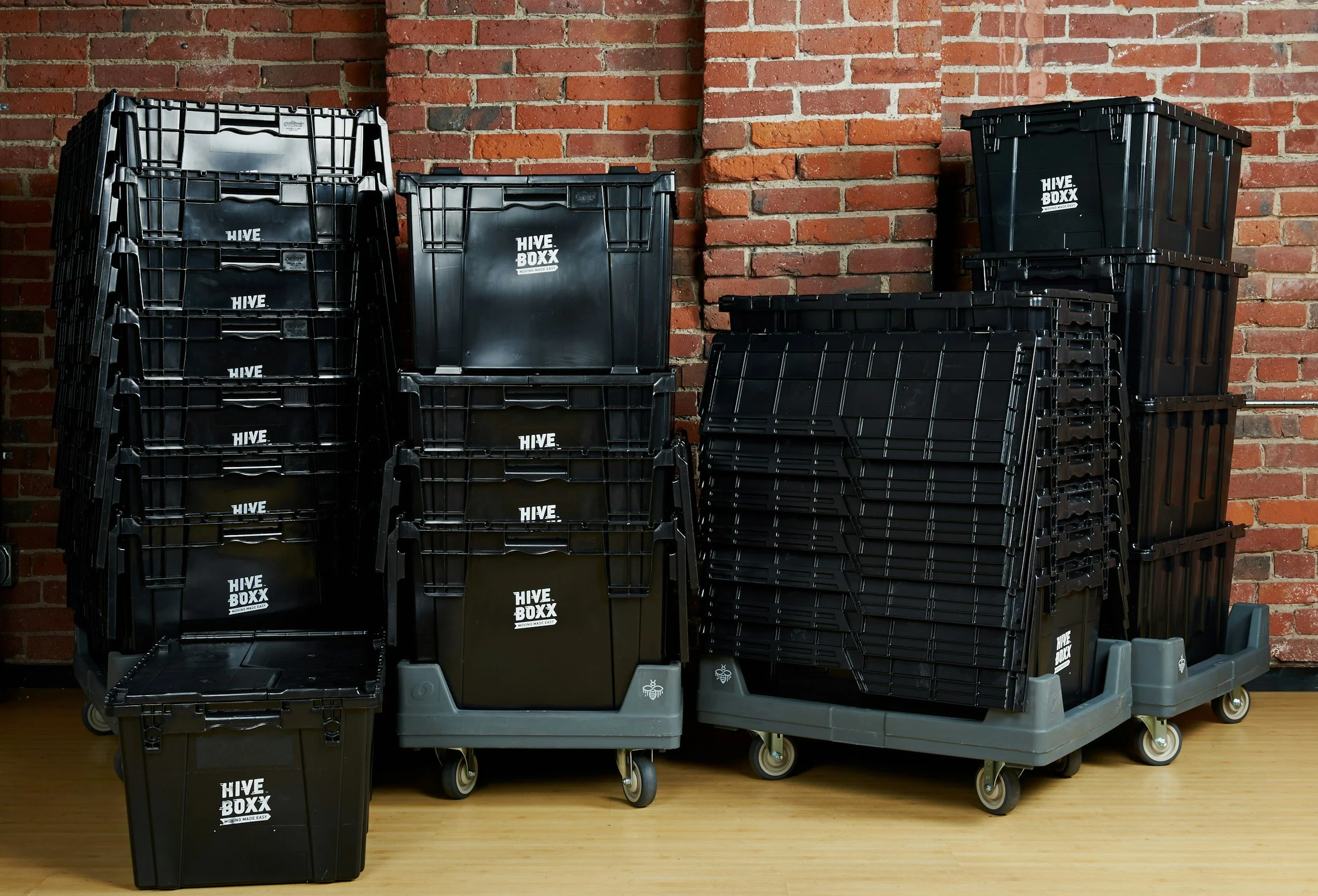 Stacked black plastic crates with the label 'HIVE BOXX' on a wheeled platform against a brick wall.