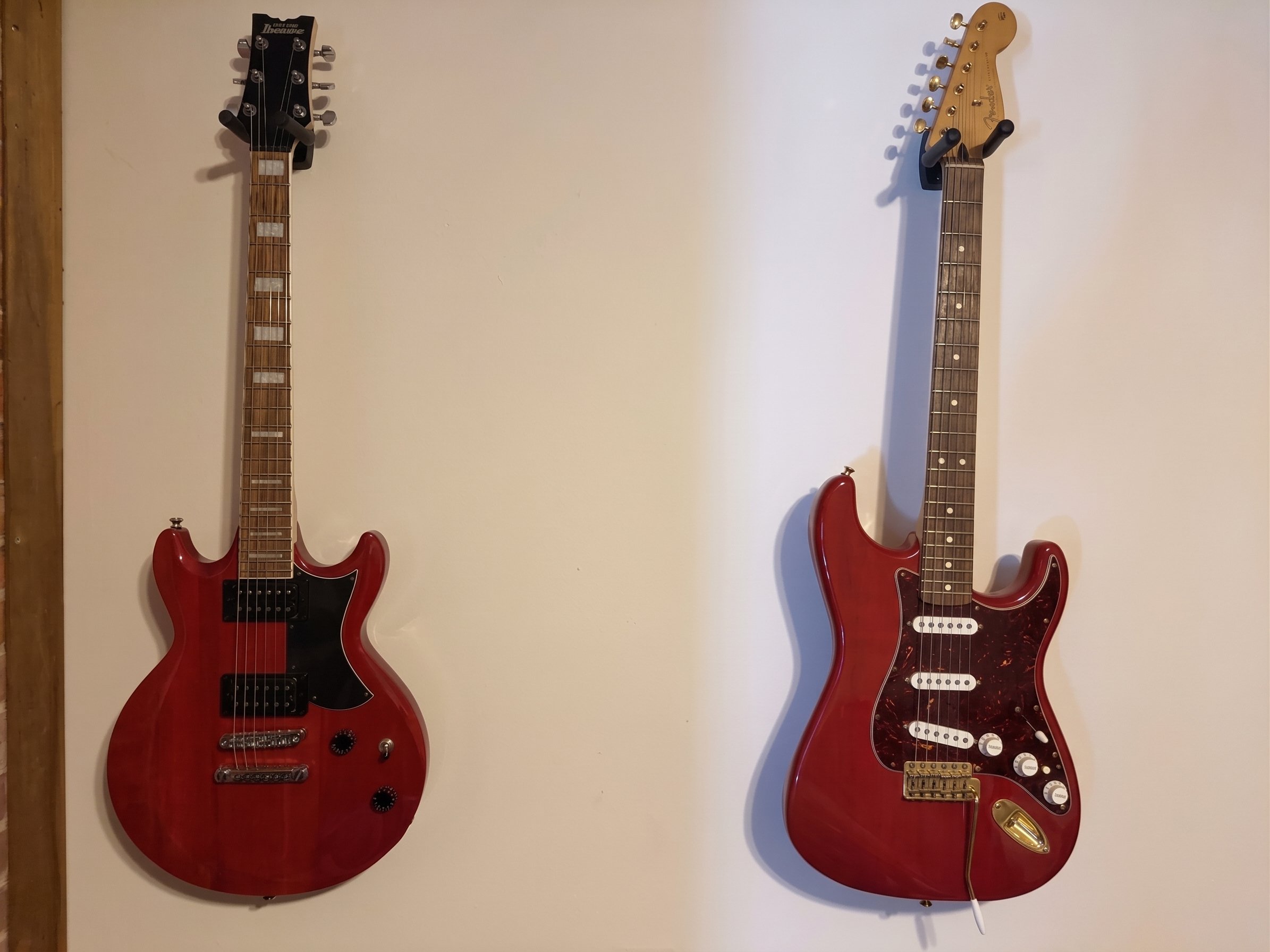 Two red electric guitars mounted on a white wall, one on the left and one on the right, with a fire extinguisher partially visible at the bottom center.