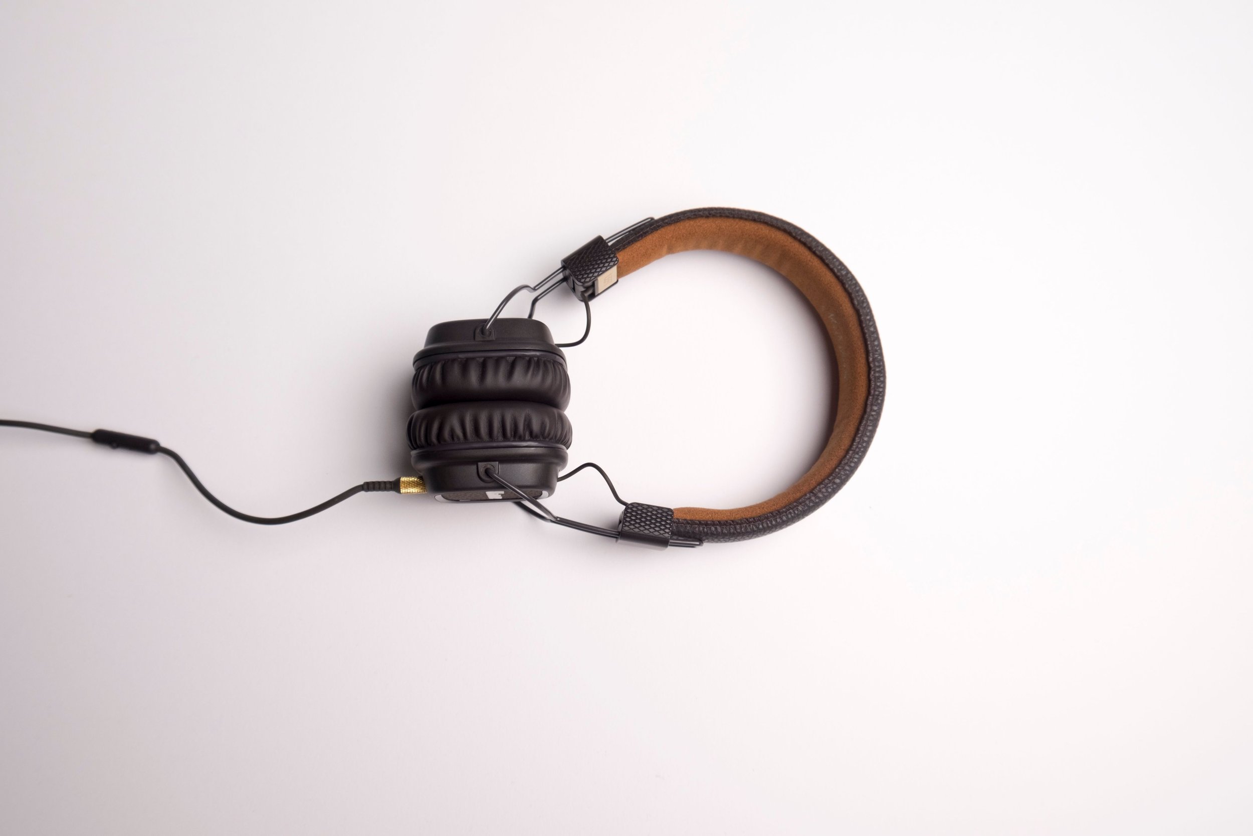 Over-ear headphones with black ear cups and a brown leather headband resting on a white surface.