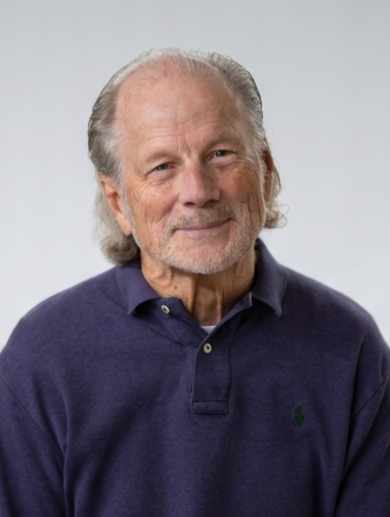 Portrait of an elderly man with gray hair and beard, wearing a navy blue polo shirt, against a plain light background.