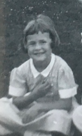 A young girl with short hair smiling and making a peace sign gesture with her hand.