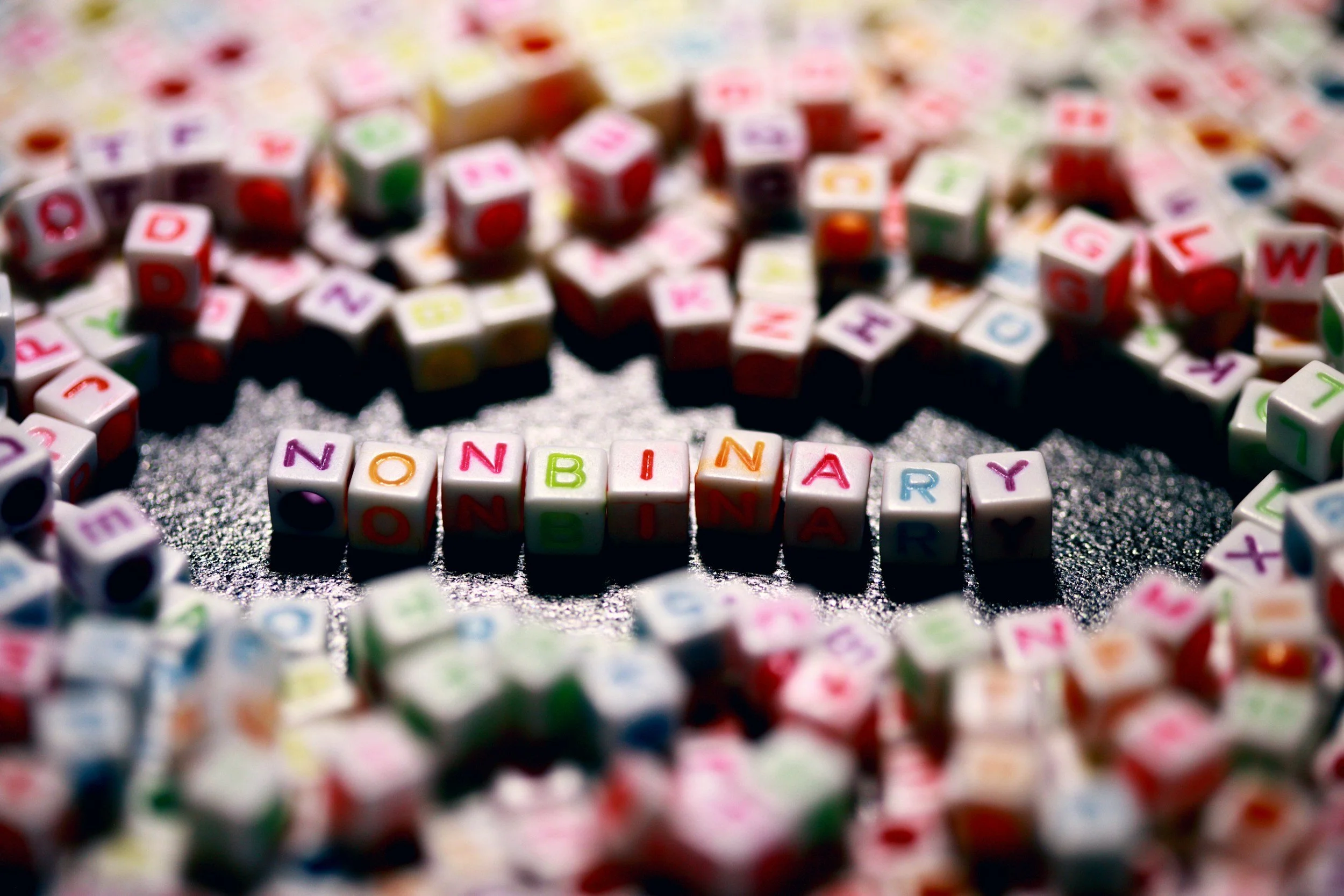 Colorful alphabet beads spell out the word 'BONBONARY' on a black surface, with scattered similar beads crawling in the background.