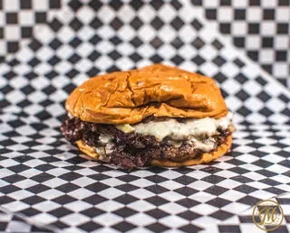 A dessert sandwich with a cookie and ice cream, topped with a dollop of whipped cream, on checkered paper.