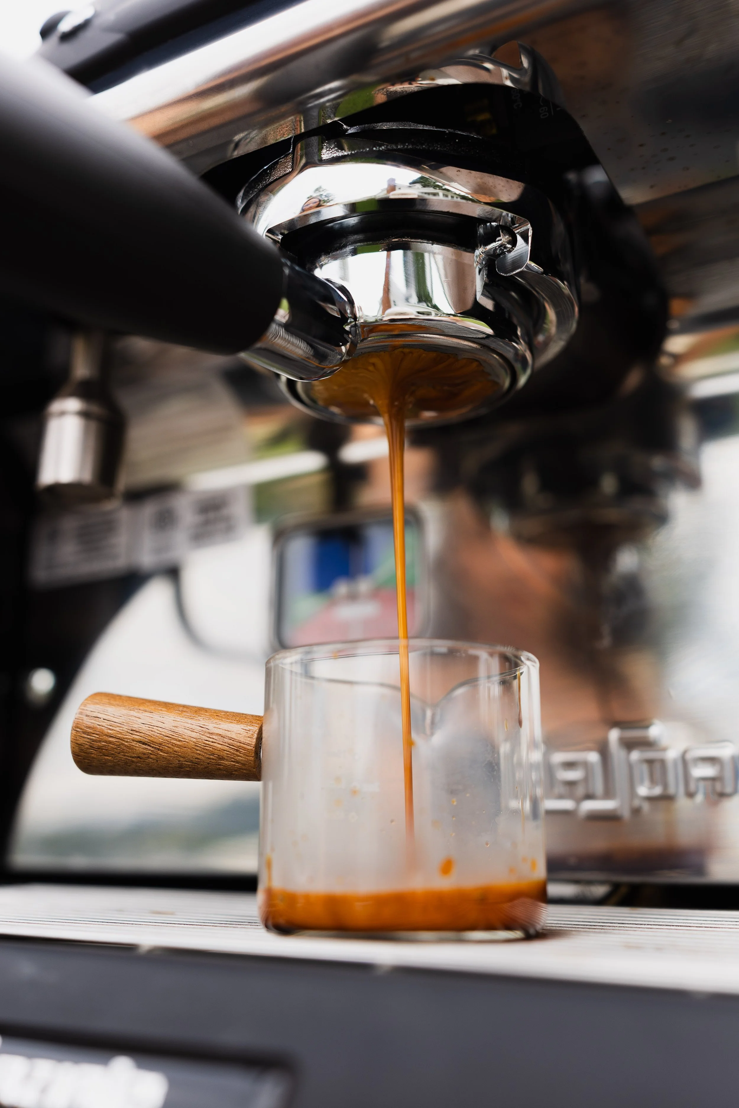 Close-up of an espresso machine pouring espresso coffee into a glass cup on a wooden surface.