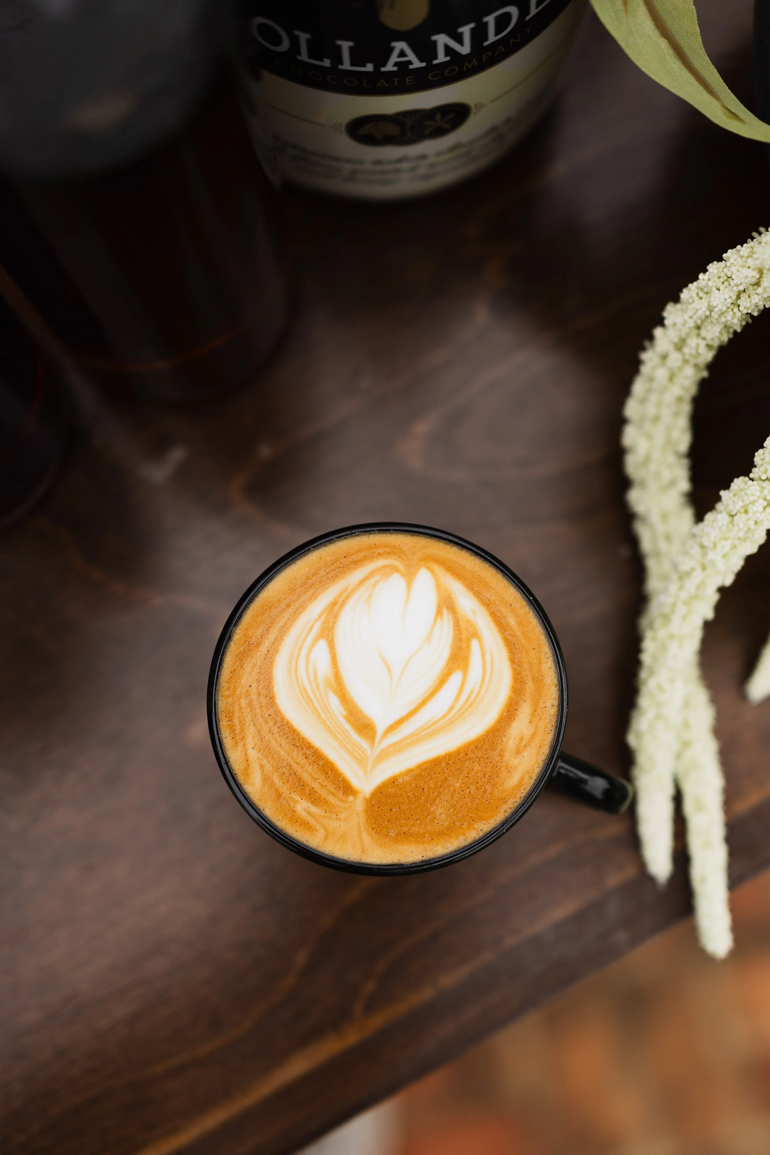 Latte with rosetta latte art on a wood table beside white wedding florals