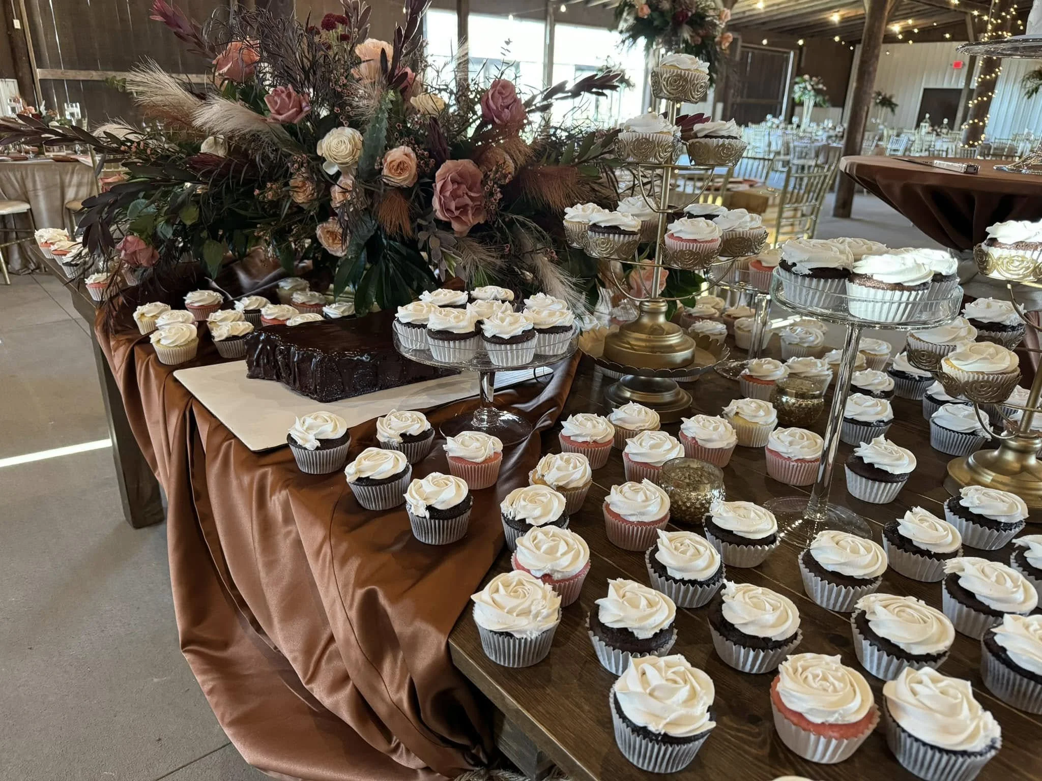 Table decorated for a celebration with a large floral centerpiece and cupcakes with rosette frosting on tiered stands and the table.