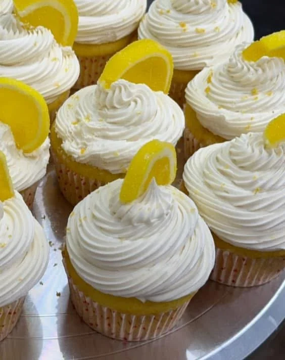 Lemon cupcakes with white frosting and lemon slices on top.