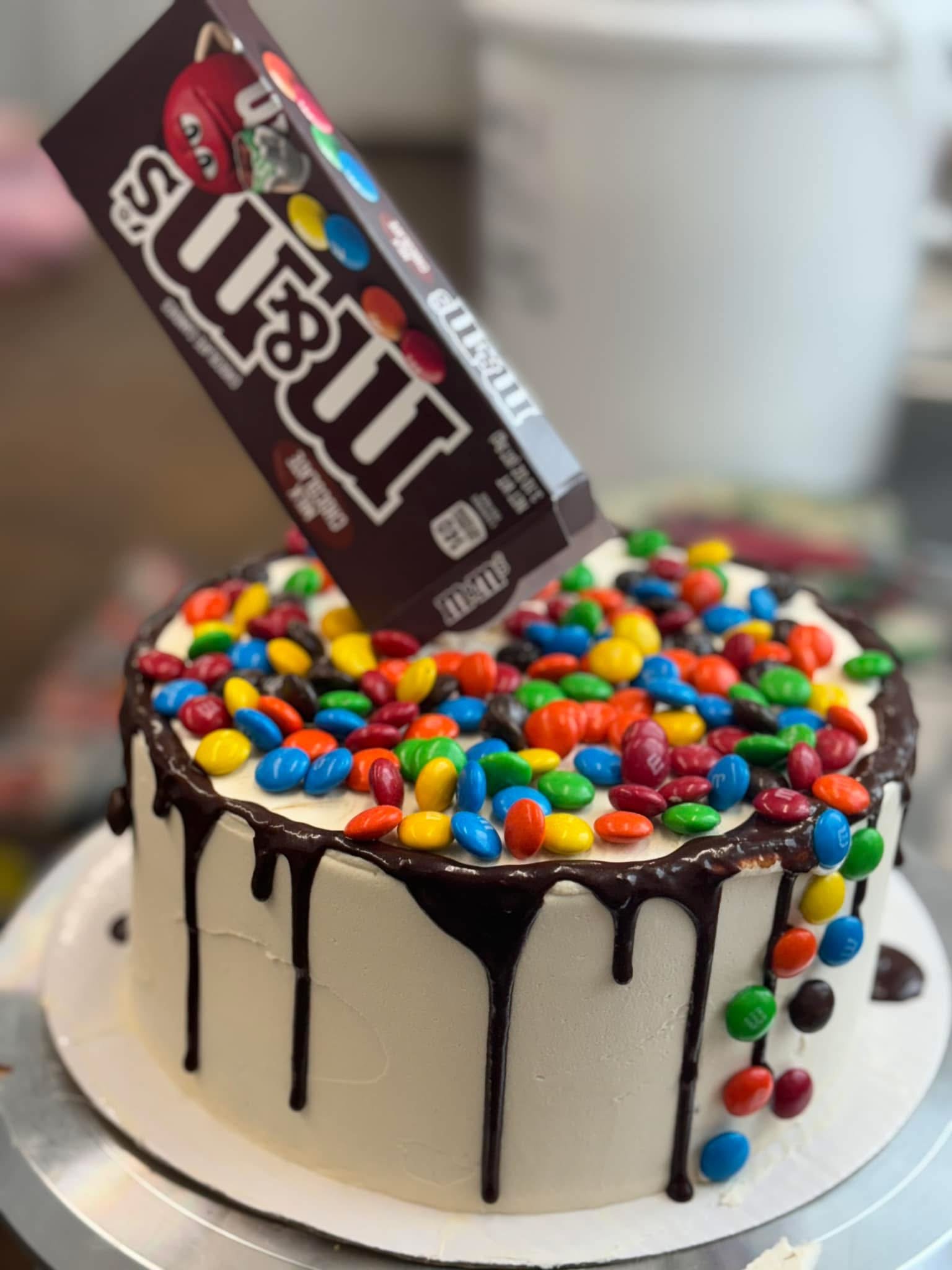 A birthday cake decorated with M&M's candies on top and chocolate drizzle hanging down the sides.