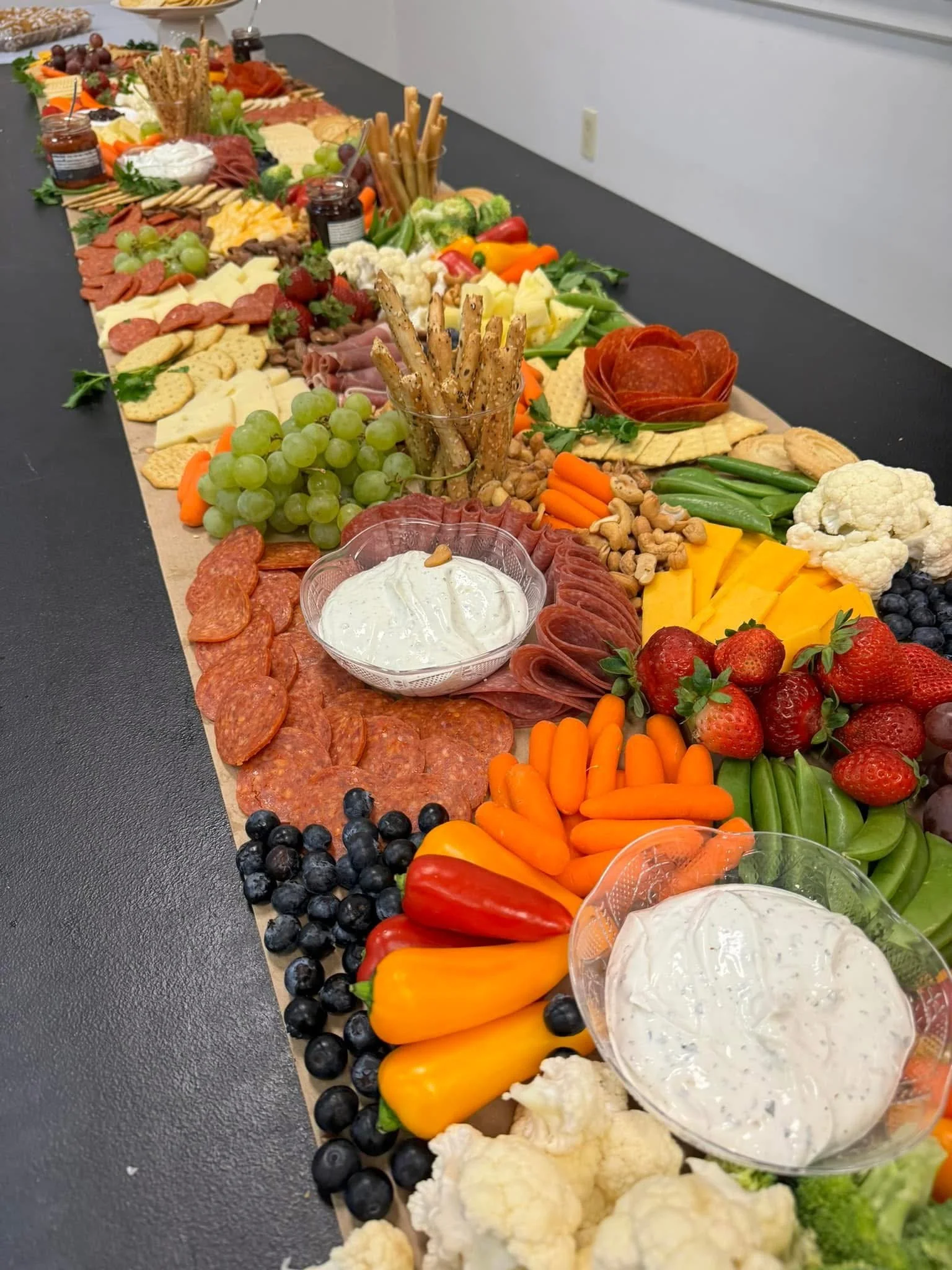 A long table with an assortment of fruits, vegetables, cheeses, meats, crackers, and dips arranged for a buffet.